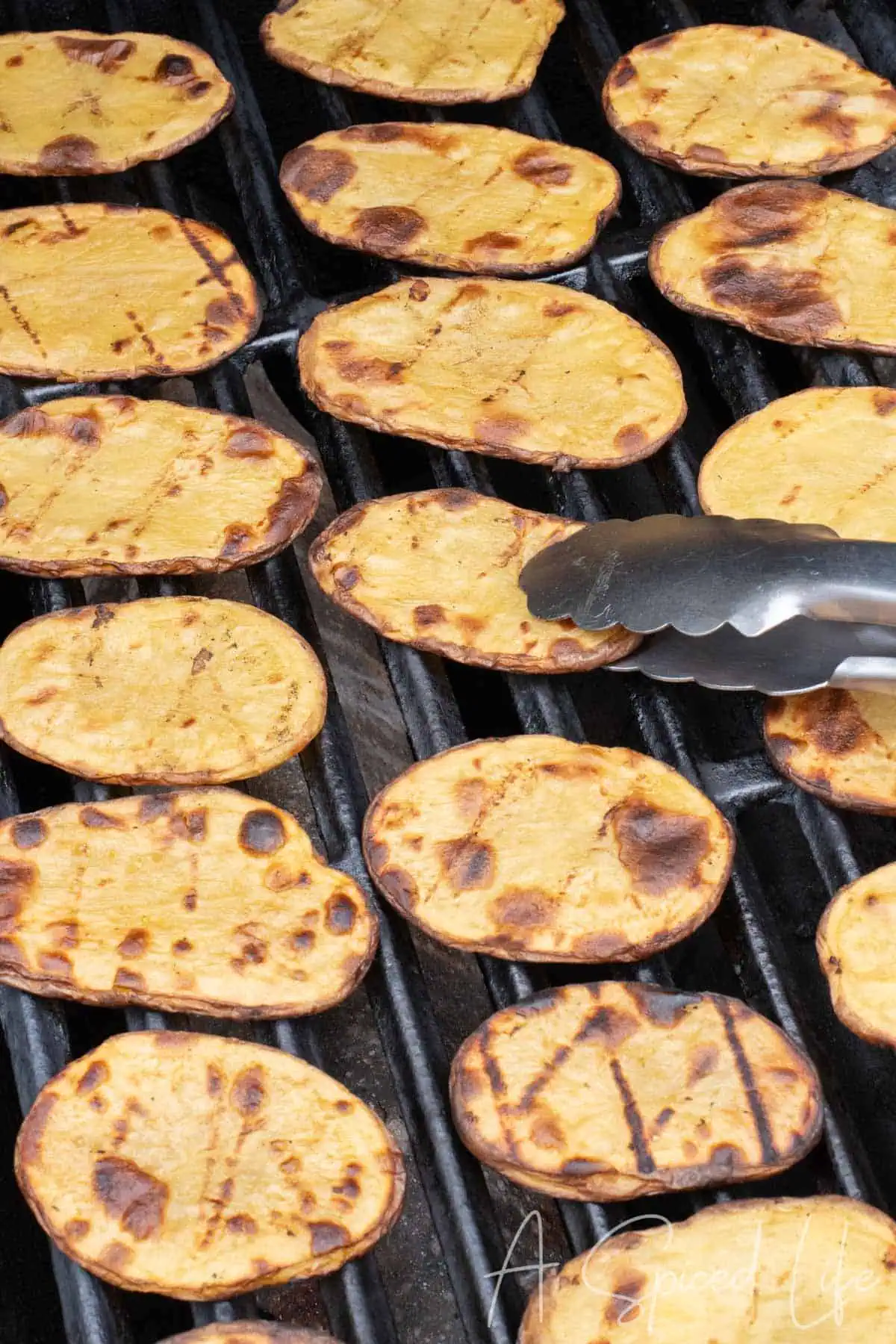 Grilled potato slices with golden edges cooking on an outdoor grill.
