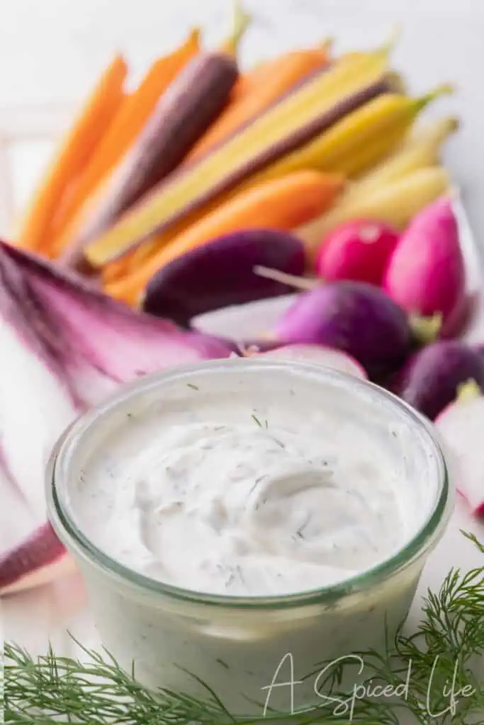 Creamy yogurt dip with fresh dill and colorful vegetables in the background