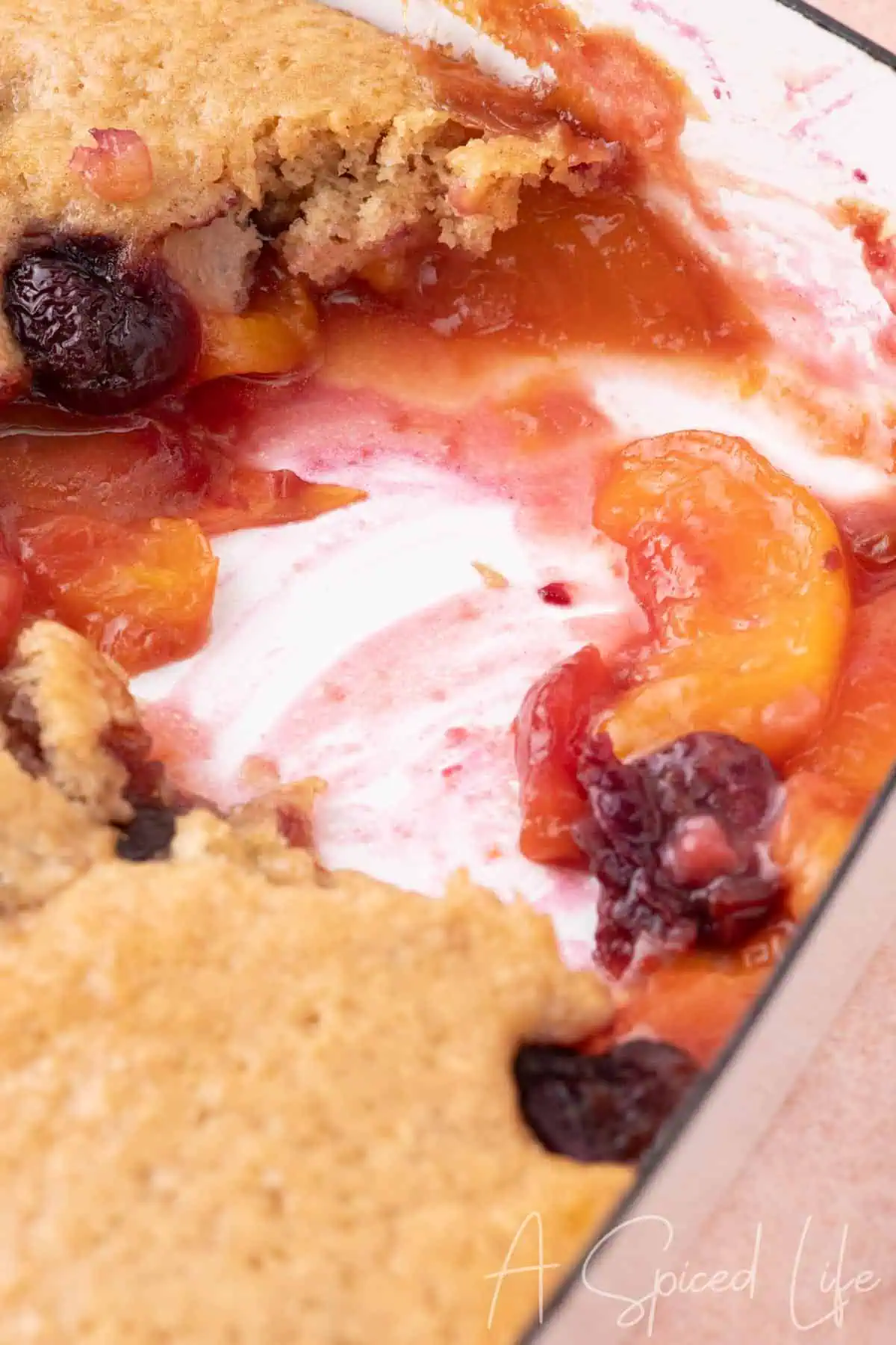 A close-up of homemade cherry peach cobbler with juicy fresh peaches and sweet cherries bubbling beneath a golden, buttery biscuit topping in a baking dish.