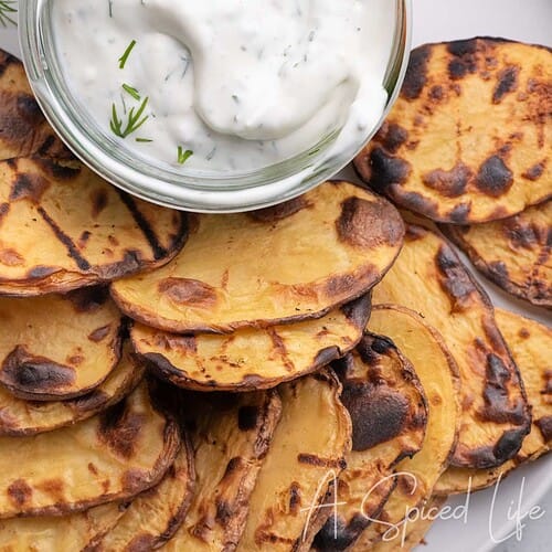 Grilled potato slices served on a platter with creamy Greek yogurt dill dip.
