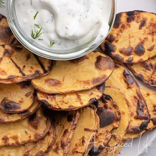 Grilled potato slices served on a platter with creamy Greek yogurt dill dip.