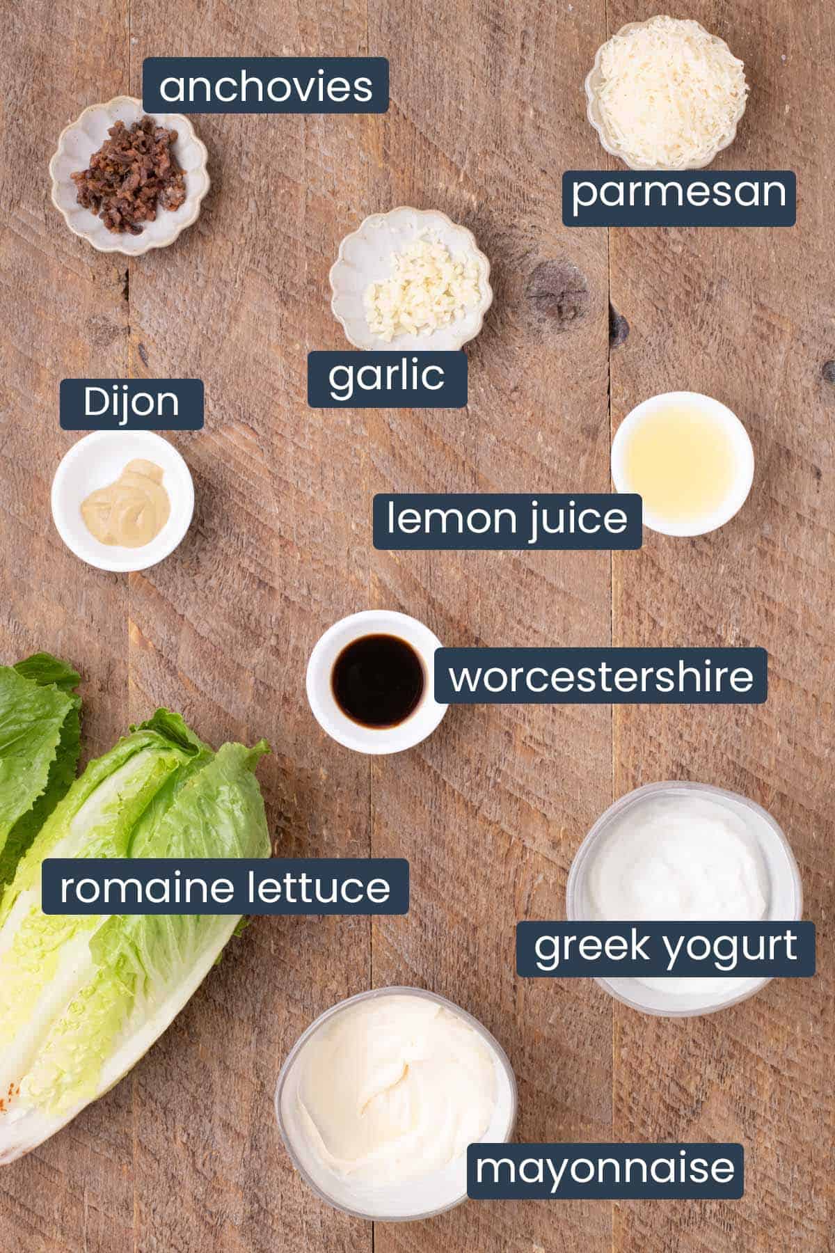 Ingredients for a light Caesar salad including romaine lettuce, mayonnaise, Greek yogurt, anchovies, Parmesan, garlic, Dijon mustard, lemon juice, and Worcestershire sauce.