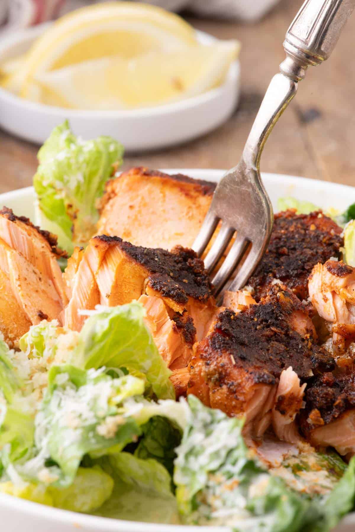 Close-up of flaky blackened salmon served over romaine Caesar salad with Parmesan cheese and creamy dressing.