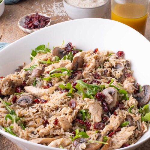 Chicken and rice salad with mushrooms, cranberries, and arugula, with apple cider-Dijon vinaigrette and rice in the background.