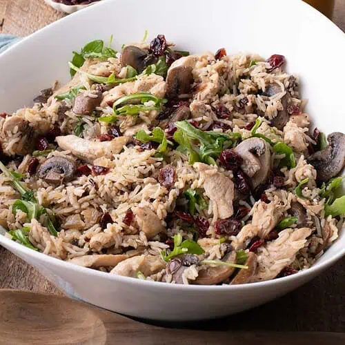 Chicken and rice salad with mushrooms, cranberries, and arugula, with apple cider-Dijon vinaigrette and rice in the background.