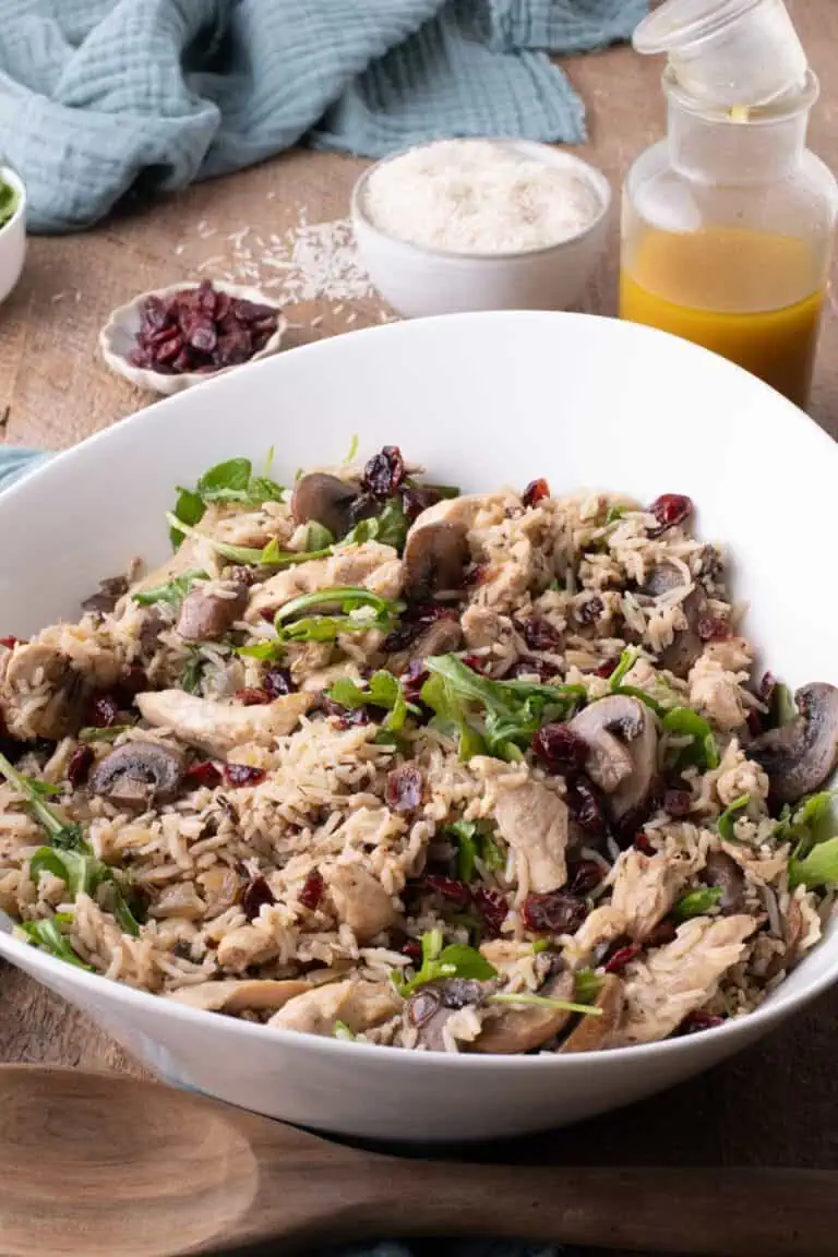 Chicken and rice salad with mushrooms, cranberries, and arugula, with apple cider-Dijon vinaigrette and rice in the background.