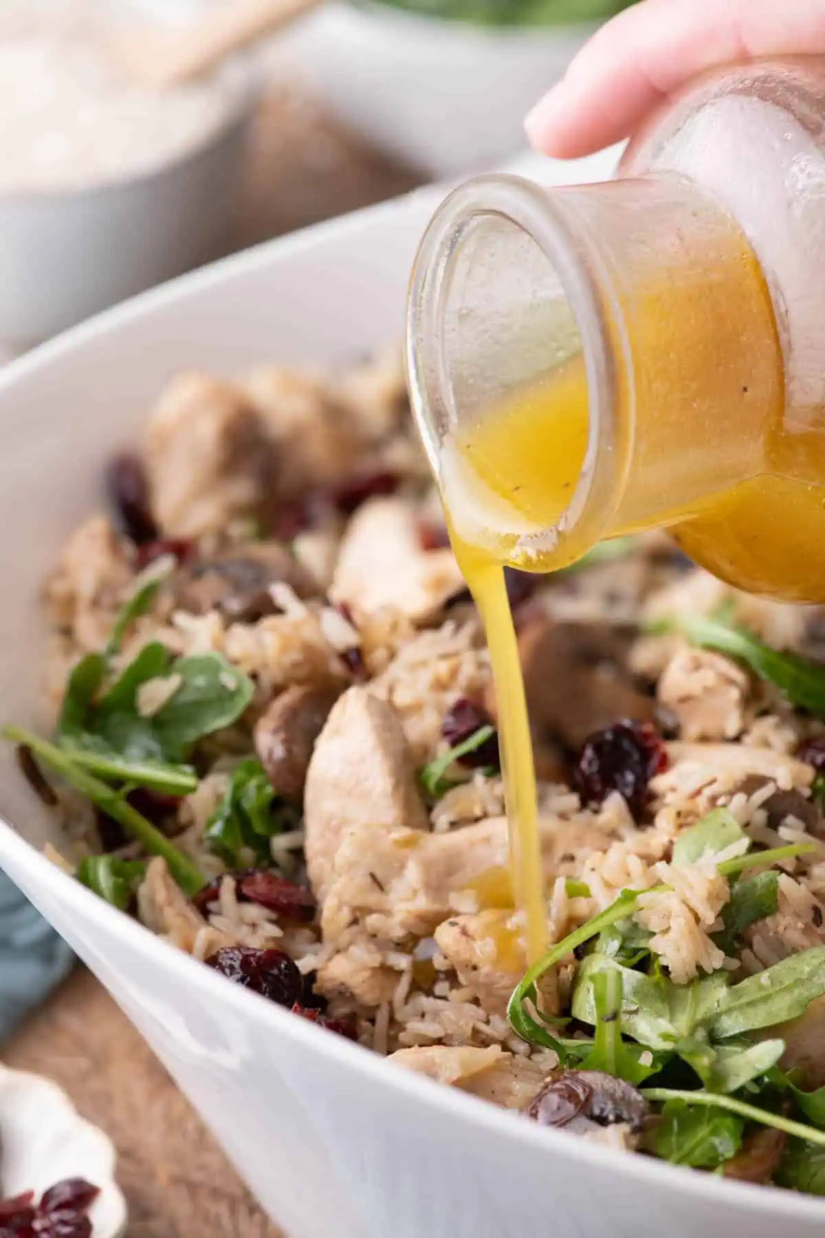 Apple cider-Dijon vinaigrette being poured over chicken and rice salad with mushrooms, cranberries, and arugula.