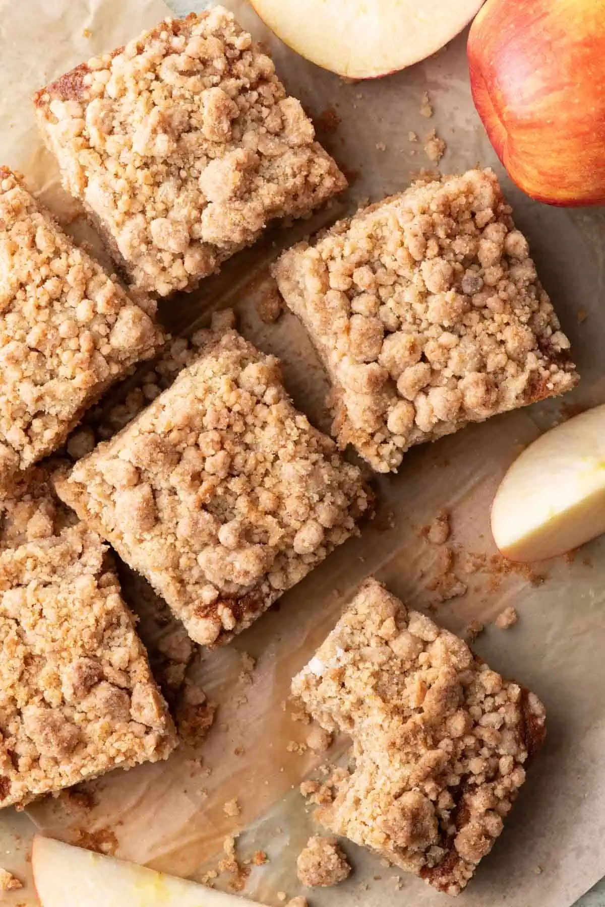 Overhead view of applesauce crumb cake squares arranged on parchment paper with whole and sliced apples.