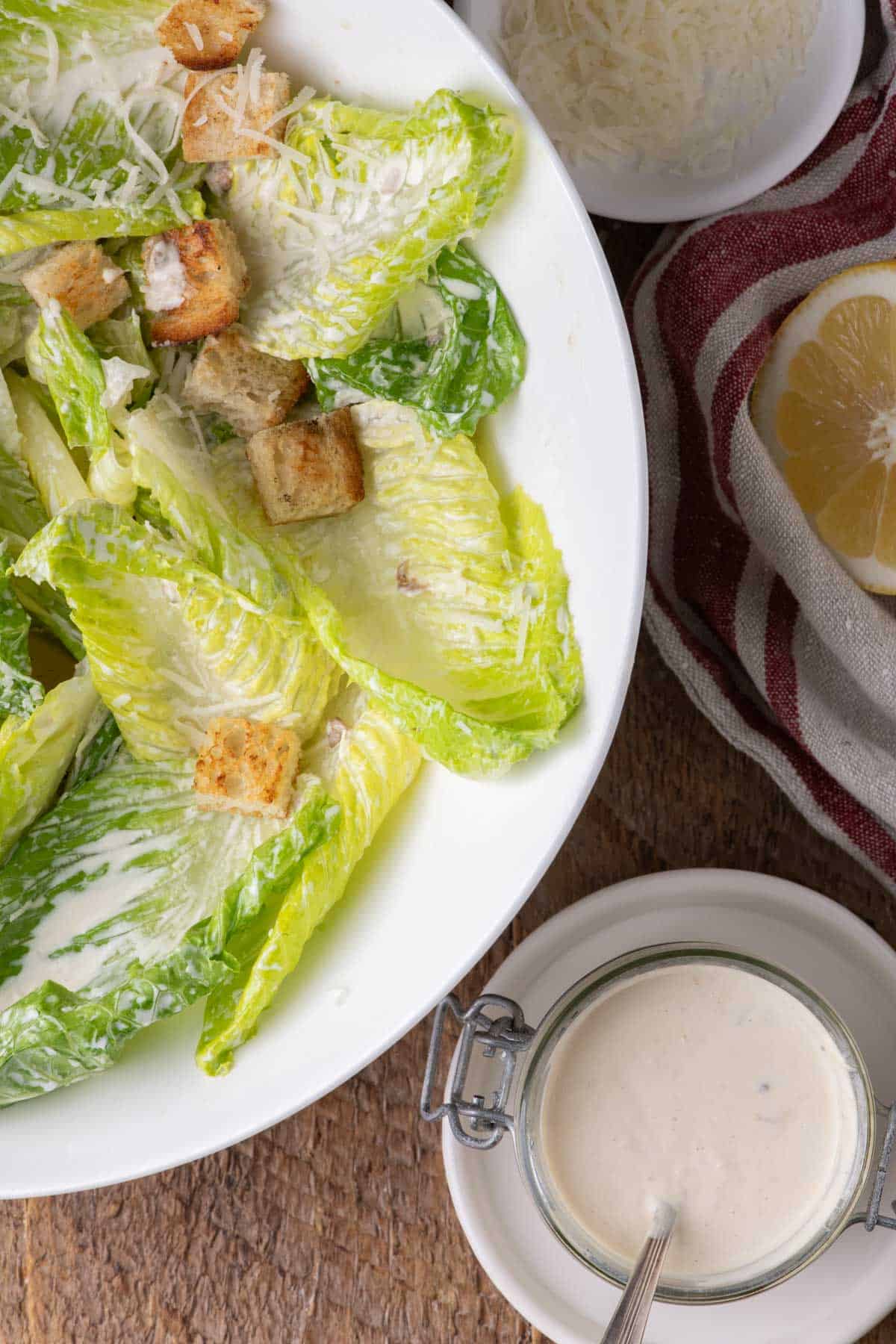 A lighter Caesar salad in a white serving bowl with croutons, Parmesan, and creamy Caesar dressing on the side.