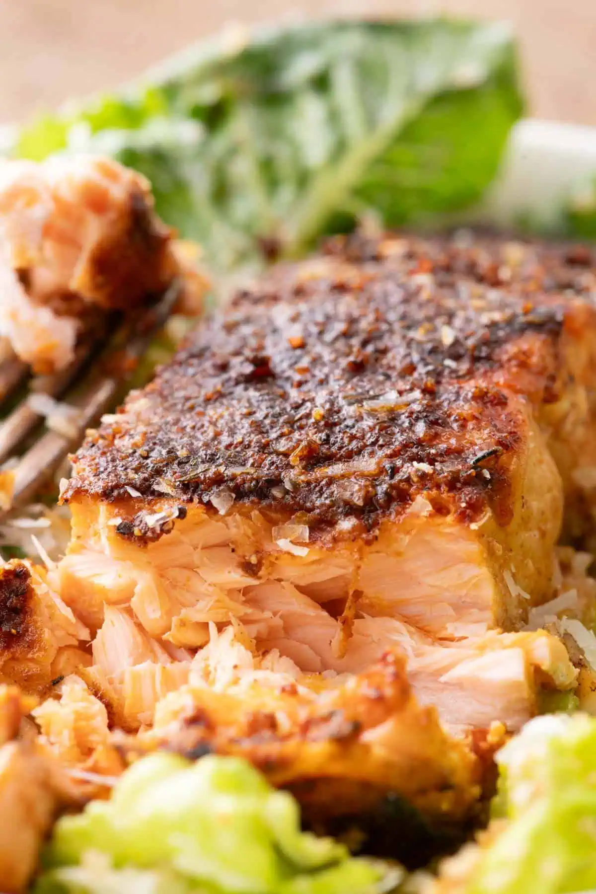 Close-up of flaky blackened salmon broken into pieces over Caesar salad.
