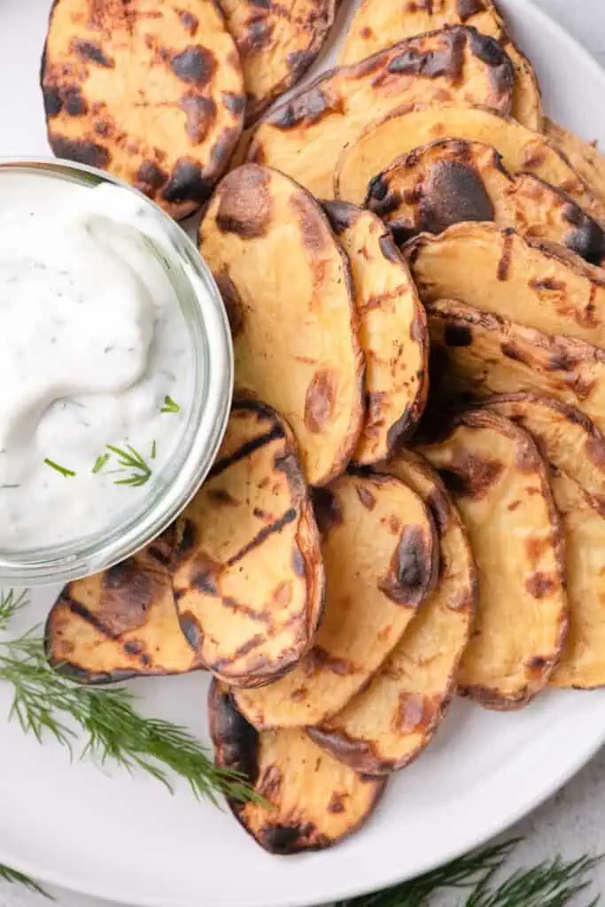 Golden grilled potato slices served on a platter with creamy Greek yogurt dill dip.