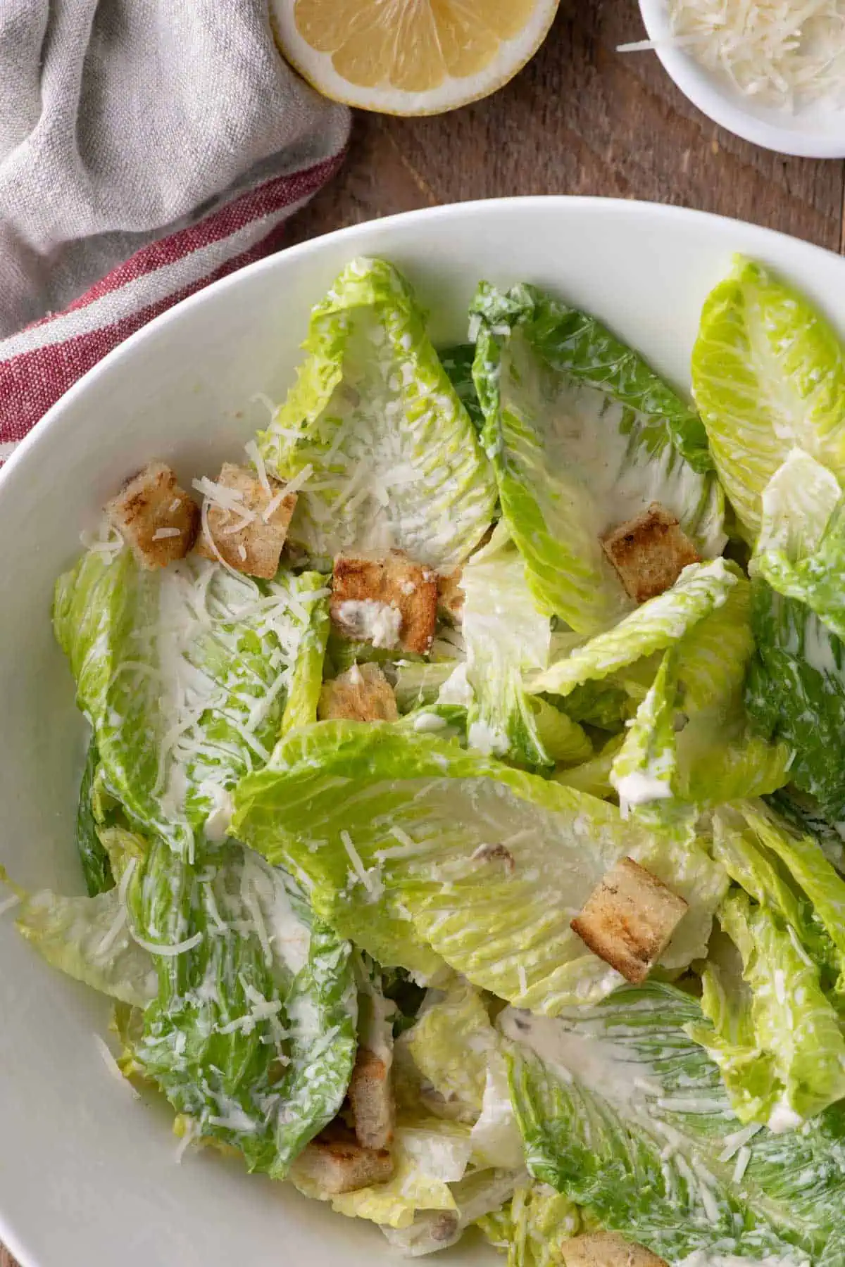 Overhead Caesar salad with creamy dressed romaine, croutons, Parmesan, lemon, and a small dish of grated cheese.