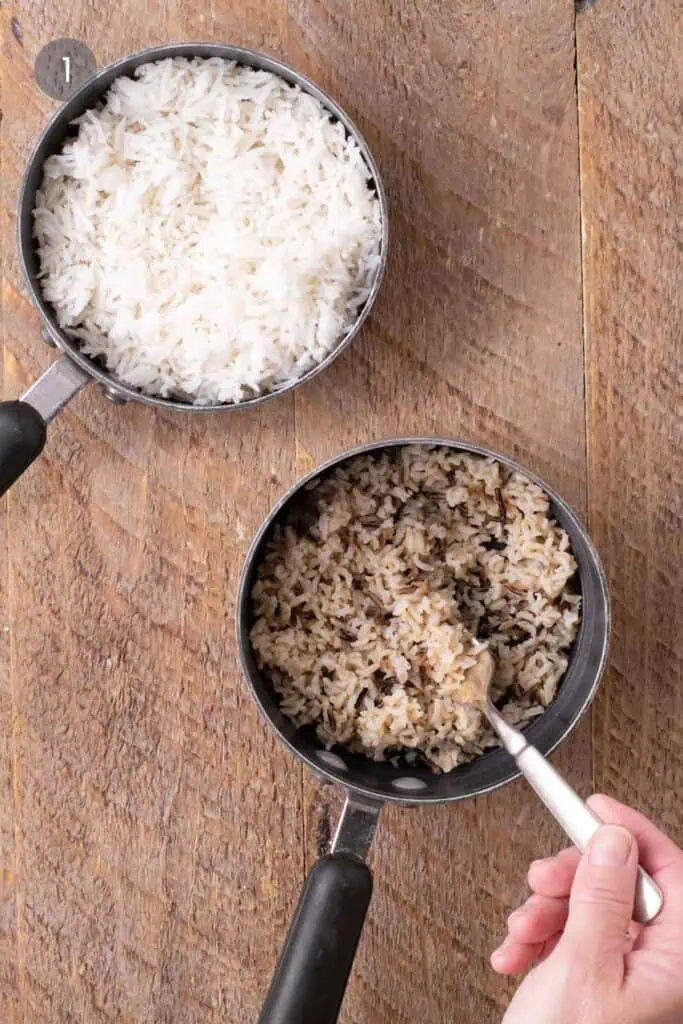 Two saucepans of cooked rice, one with white rice and one with wild rice blend, for warm chicken and rice salad.