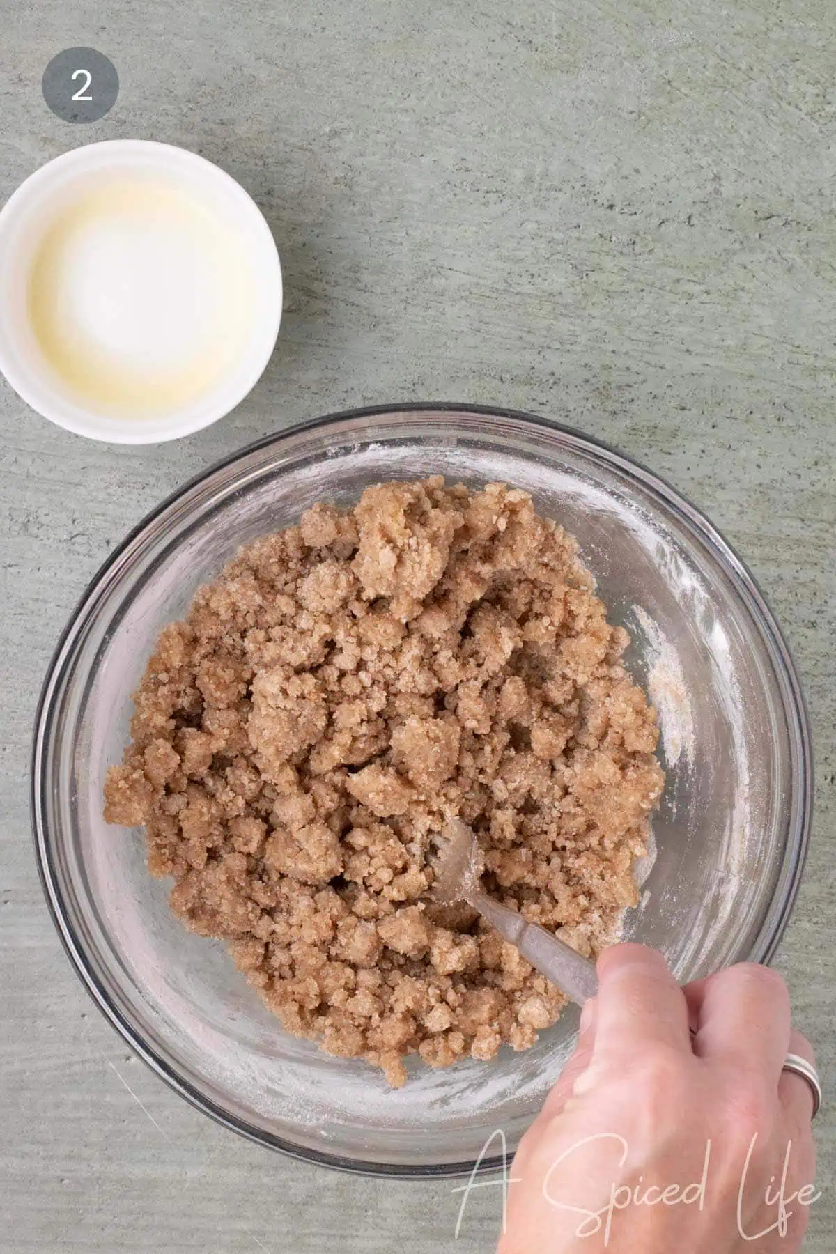 Mixed crumb topping in a glass bowl with large and small crumb pieces after the melted butter has been stirred in.
