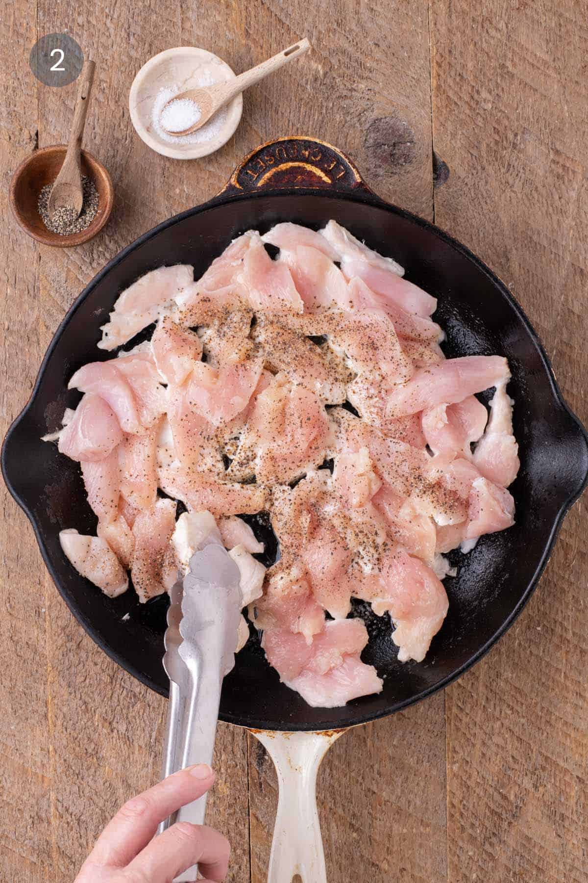 Sliced raw chicken in a cast-iron skillet seasoned with salt and black pepper for warm chicken and rice salad.