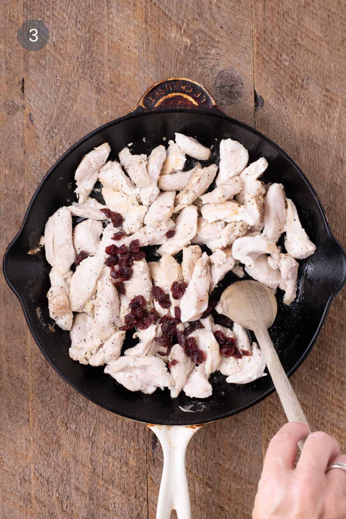 Cooked chicken strips in a skillet with dried cranberries added for warm chicken and rice salad.
