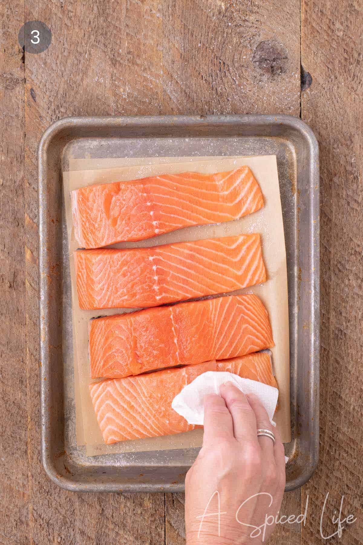 Salmon fillets being patted dry with a paper towel before seasoning.