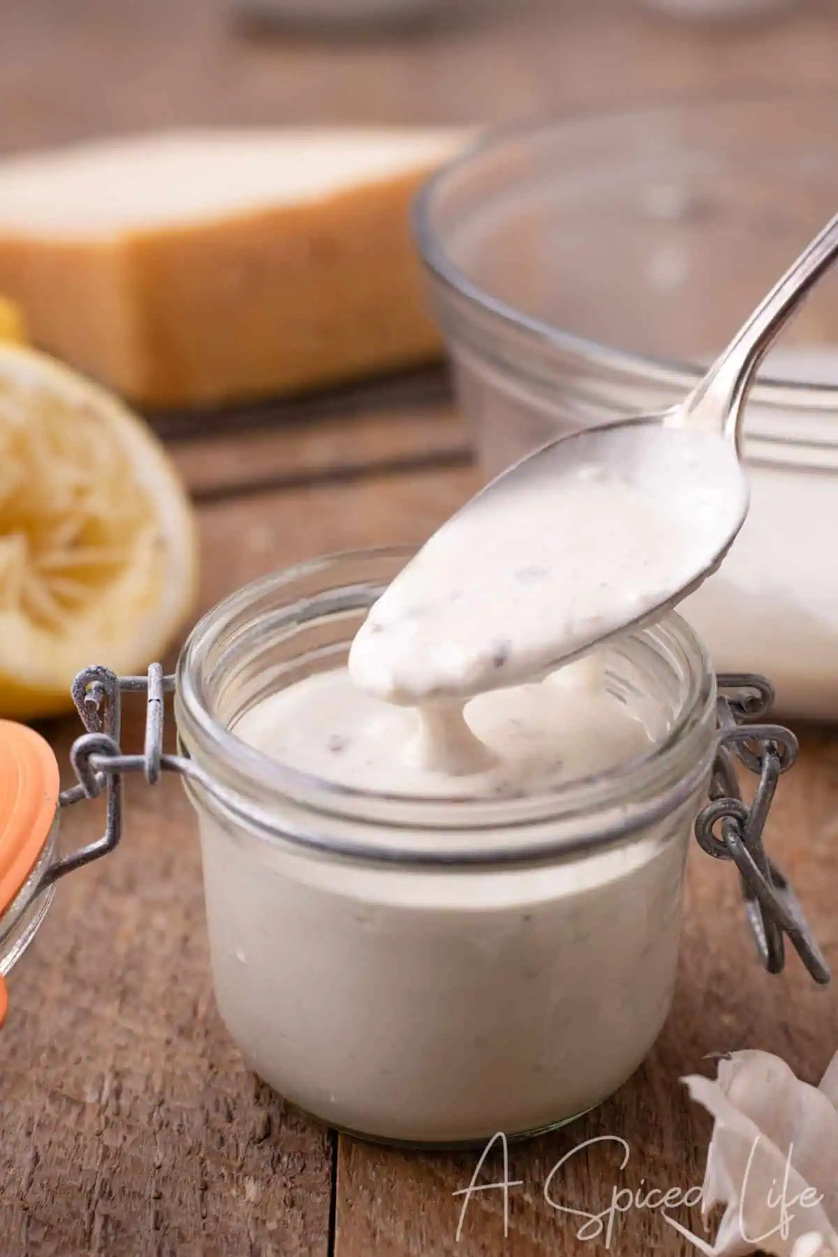 Thick creamy Caesar dressing clinging to a spoon above a small glass jar.