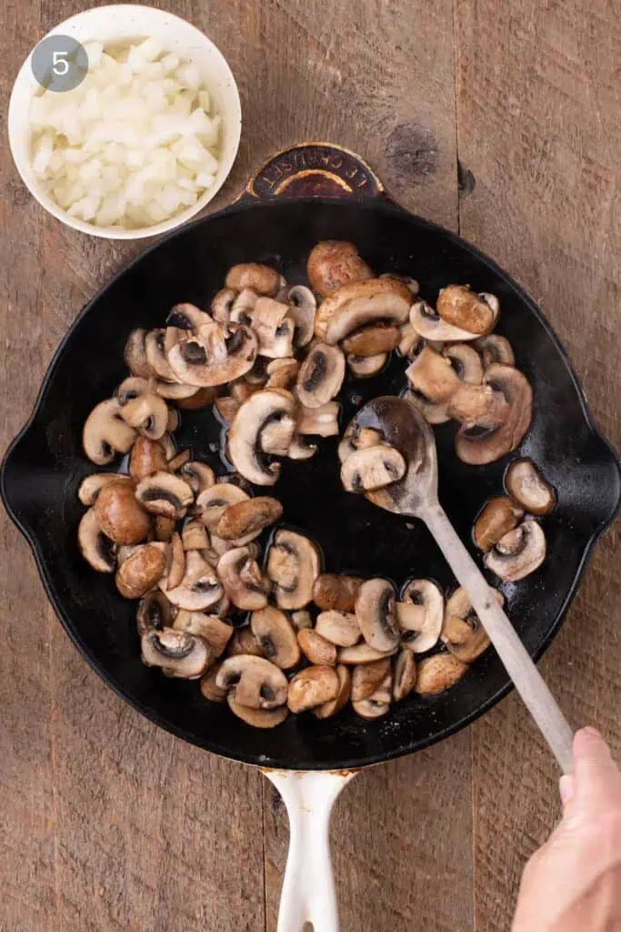 Browned mushrooms in a skillet with chopped onions ready to be added for warm chicken and rice salad.