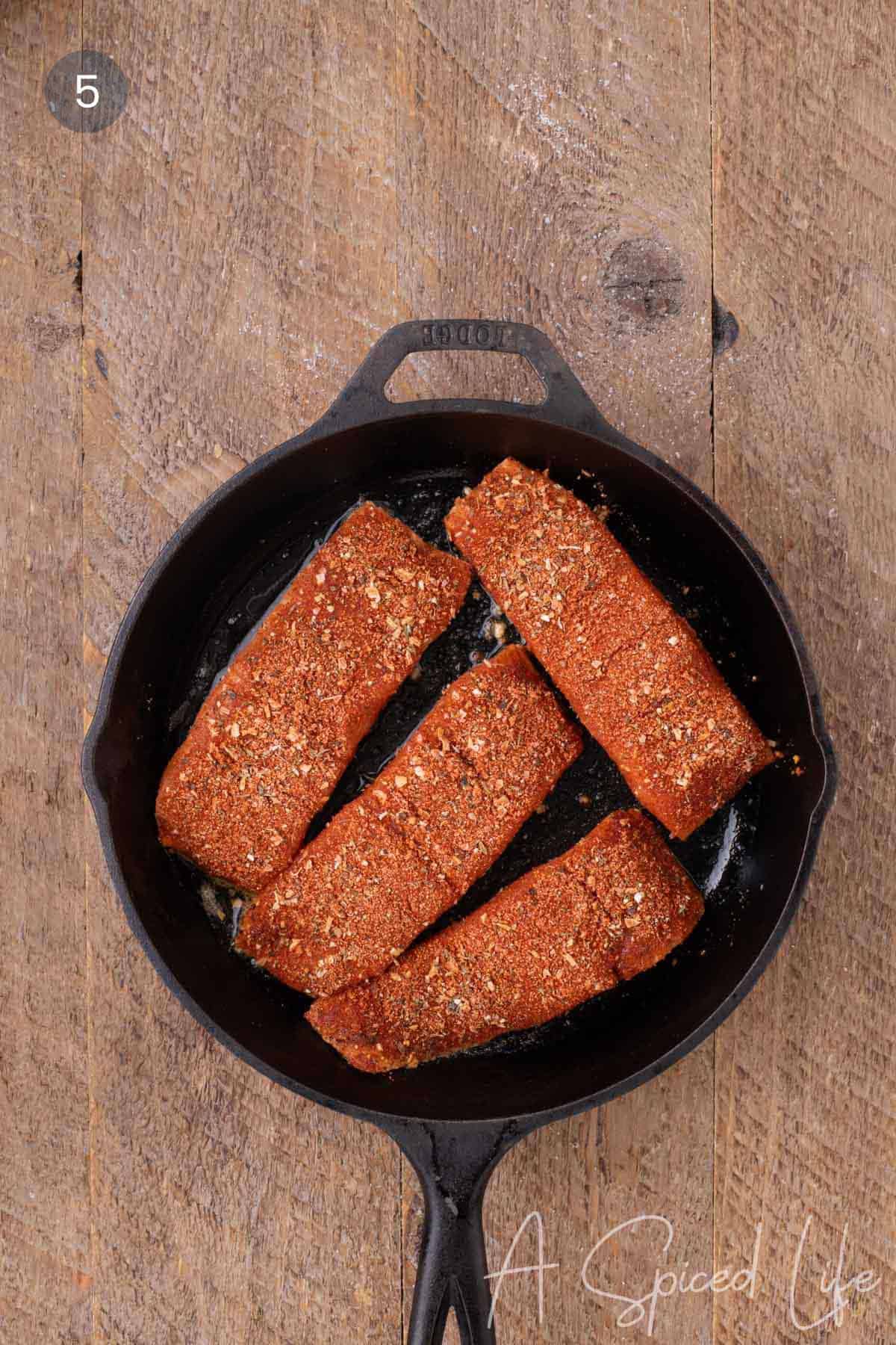Seasoned salmon fillets cooking skin-side down in a cast-iron skillet.