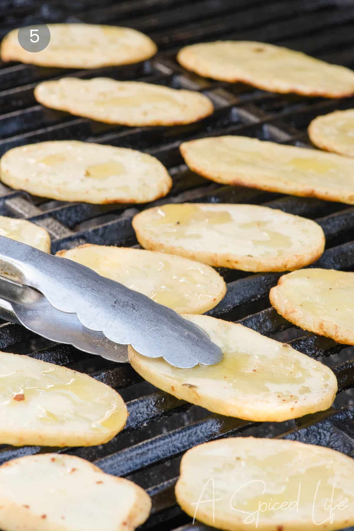 Grilled potato slices cooking in a single layer over direct heat.