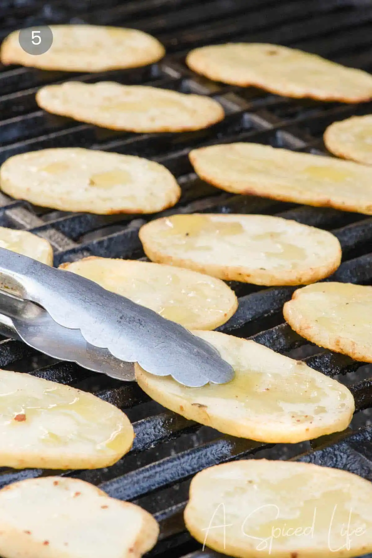 Grilled potato slices cooking in a single layer over direct heat.