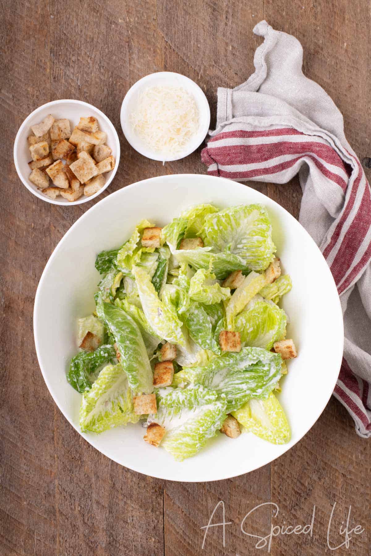 Finished Caesar salad with creamy dressed romaine, croutons and grated Parmesan in a white serving bowl.