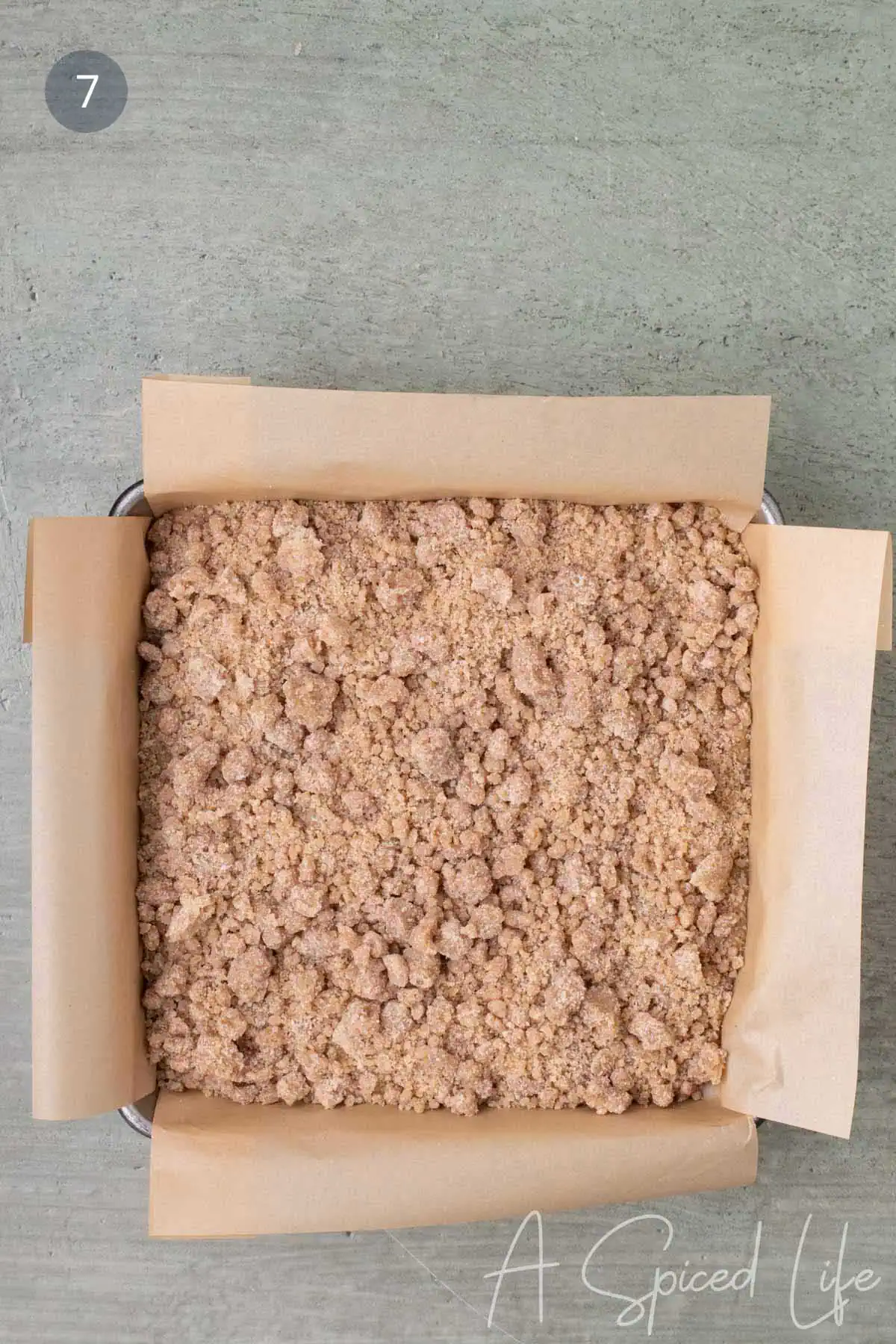 Unbaked applesauce crumb cake in a parchment-lined square pan fully covered with crumb topping and ready for the oven.