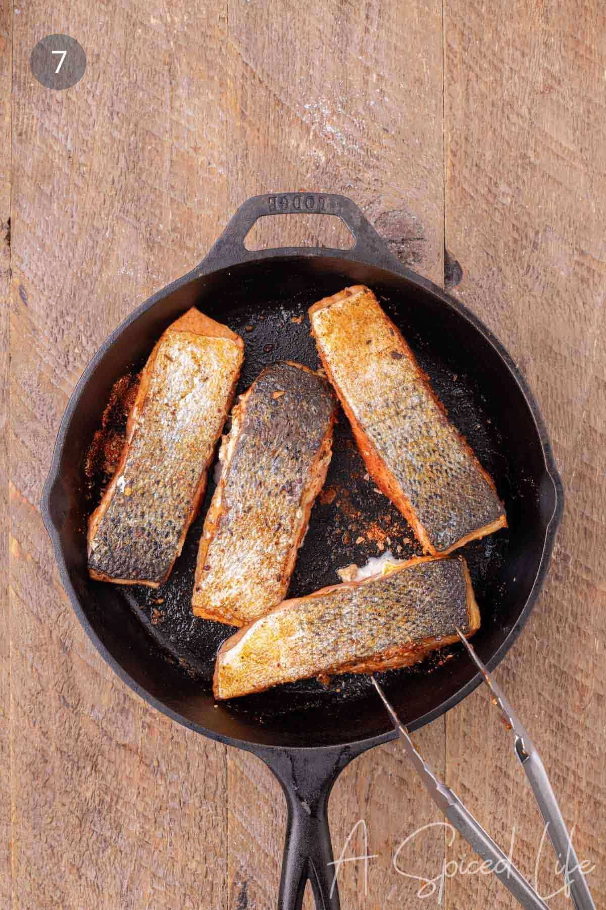 Blackened salmon fillets flipped in a cast-iron skillet to finish cooking.
