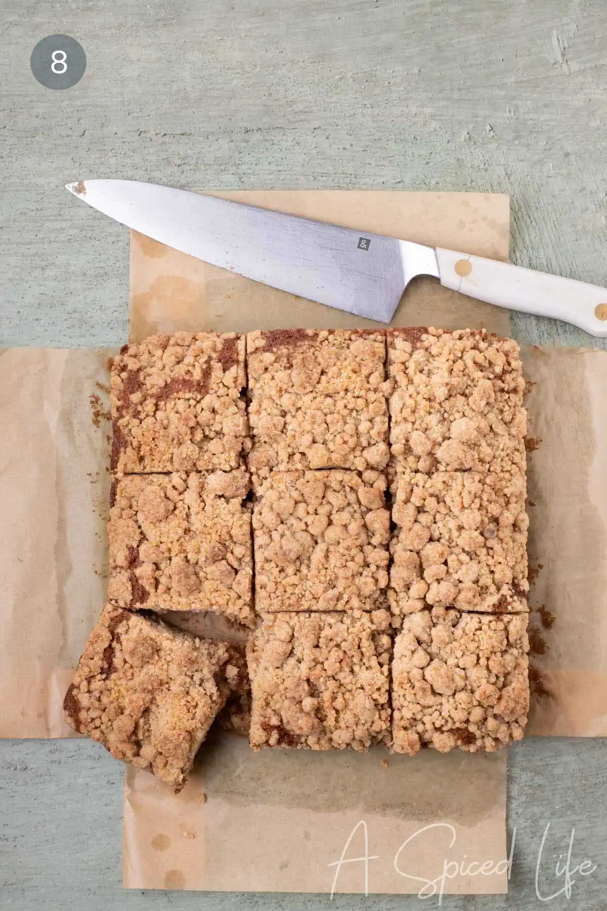 Baked applesauce crumb cake cut into squares on parchment paper with one square slightly pulled away from the pan.