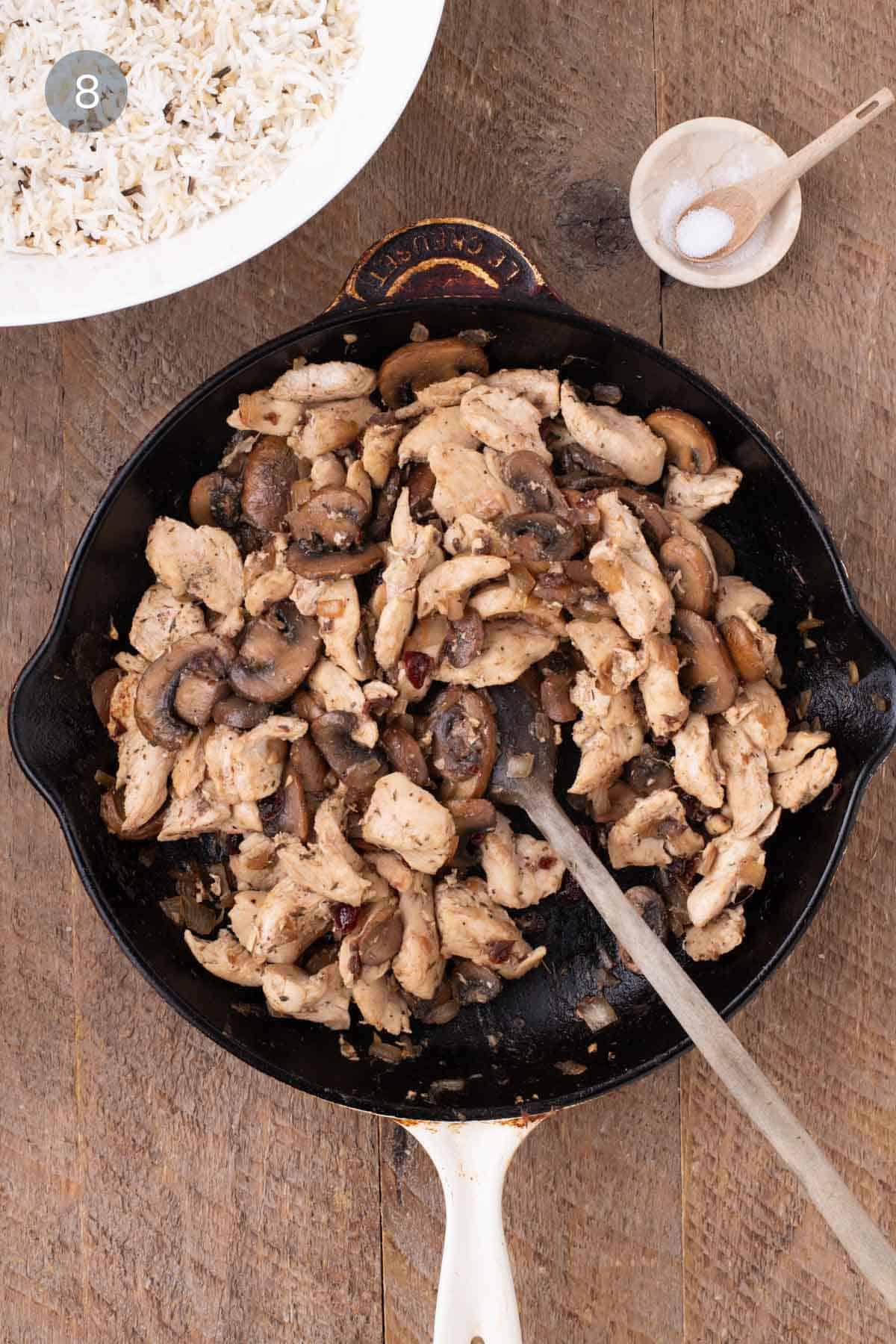 Chicken and mushroom mixture in a skillet beside a bowl of cooked rice for warm chicken and rice salad.