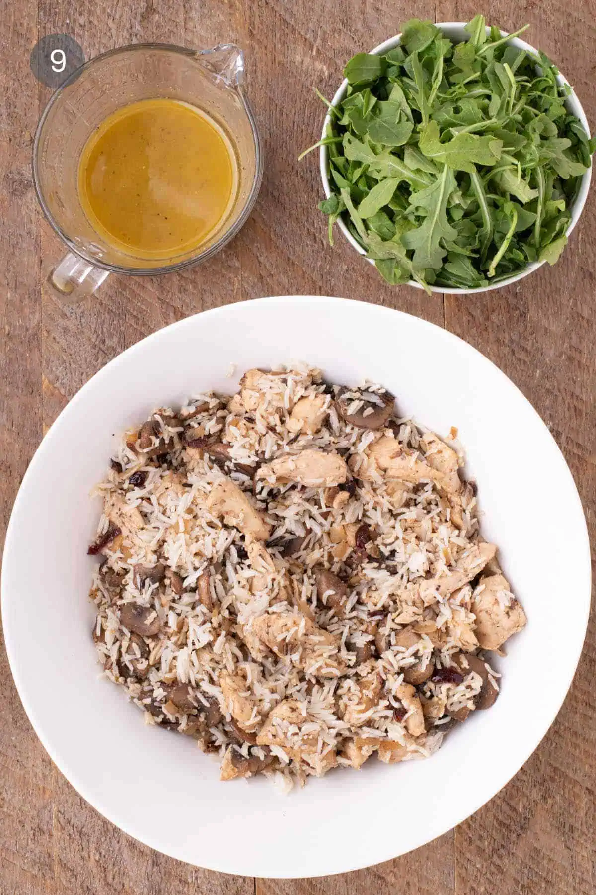 Bowl of warm chicken and rice salad with vinaigrette and baby arugula ready to be tossed in.