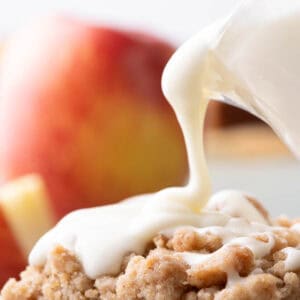 Thick cream cheese glaze being poured over applesauce crumb cake.