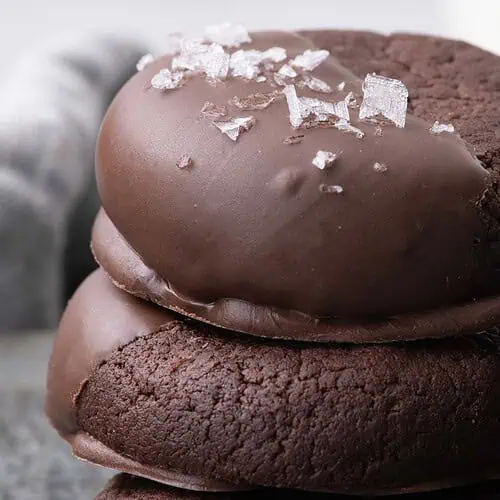 Close-up of stacked chocolate cookies half dipped in chocolate and sprinkled with flaky salt.