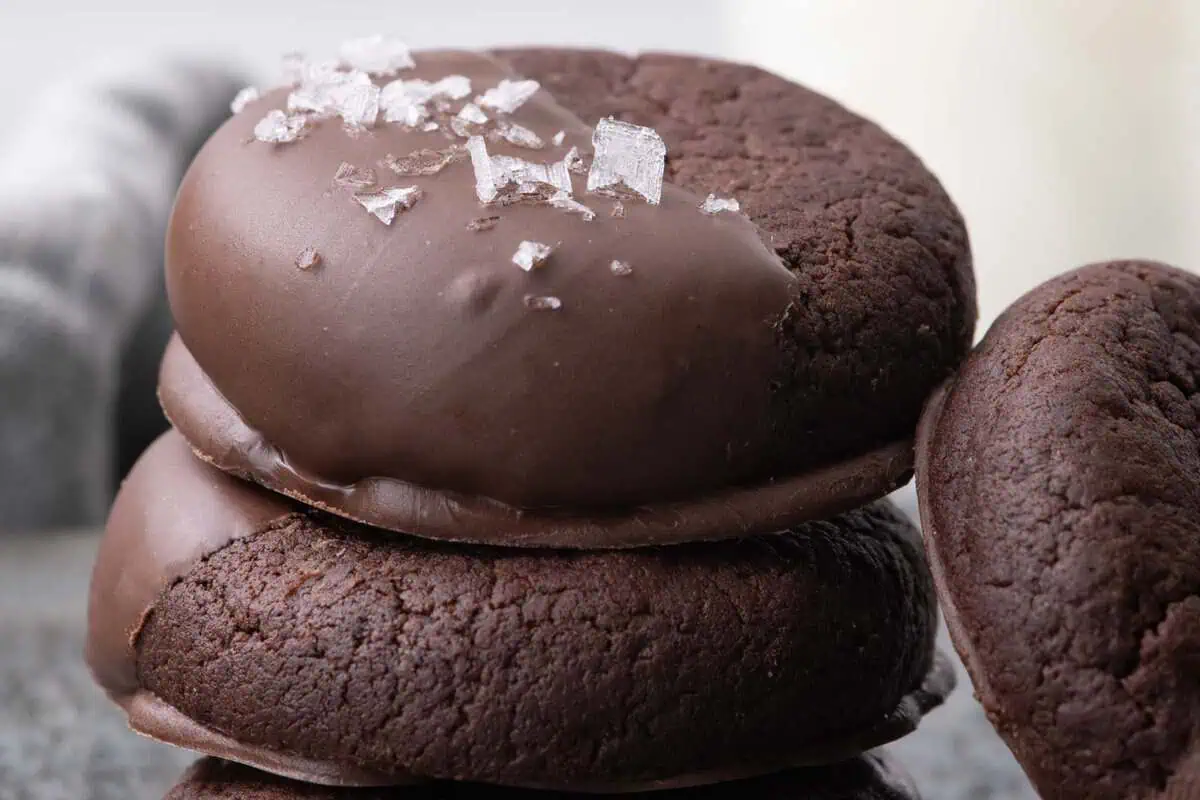 Close-up of stacked chocolate cookies half dipped in chocolate and sprinkled with flaky salt.