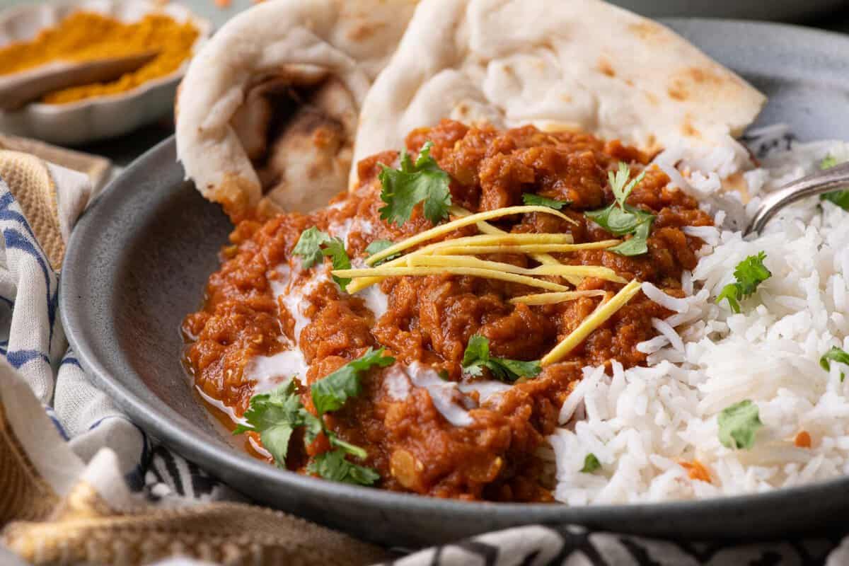 Close-up of red lentil stew with basmati rice, naan, coconut cream, cilantro, and fresh ginger