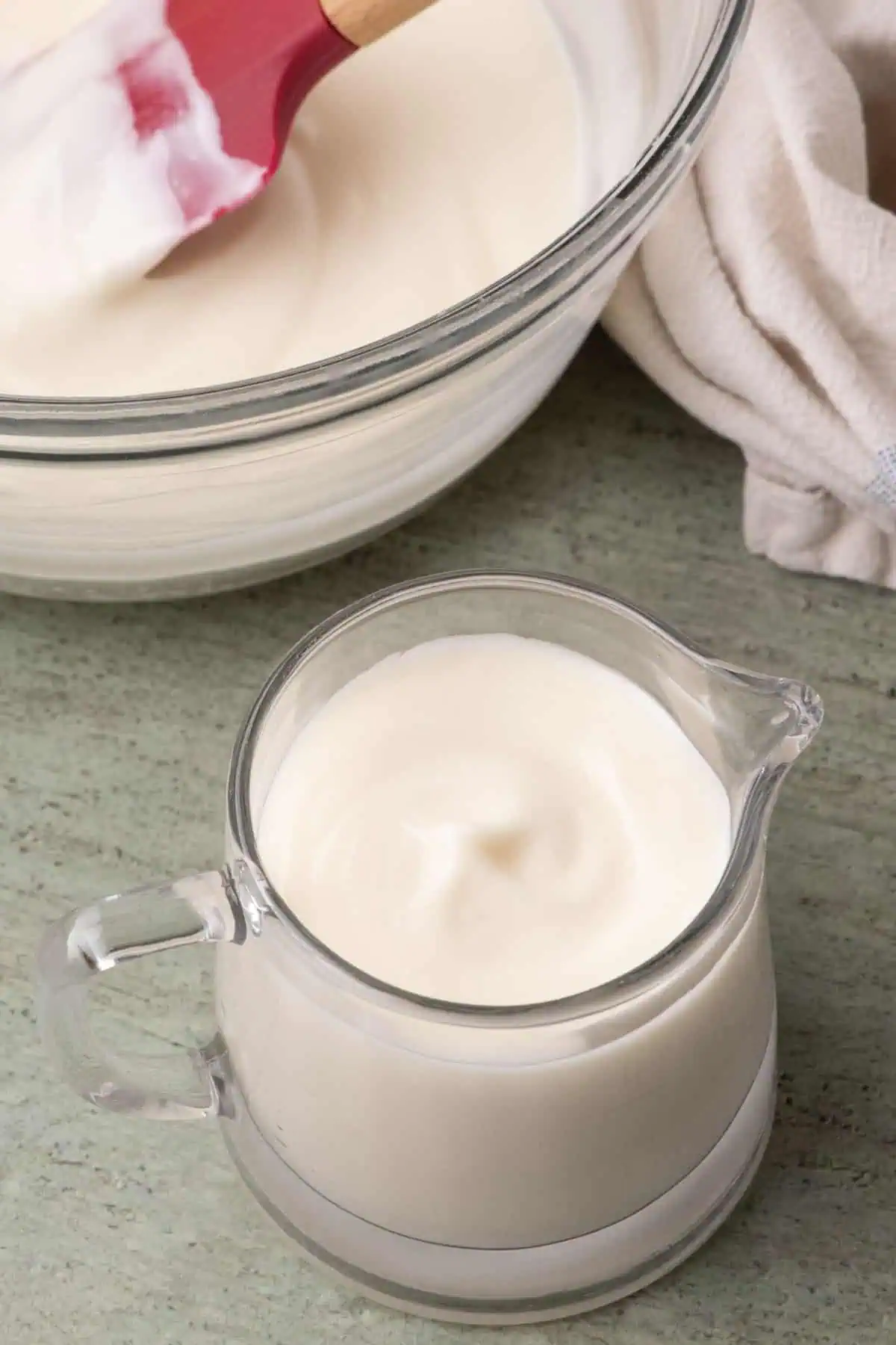 Cream cheese glaze in a small glass pitcher beside a mixing bowl.