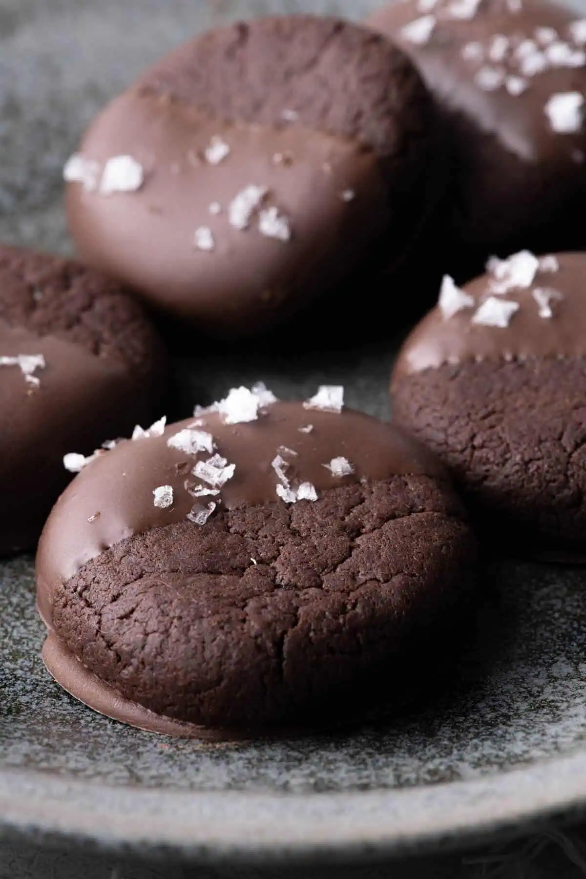 Close-up of thick chocolate cookies half coated in chocolate and sprinkled with flaky salt.