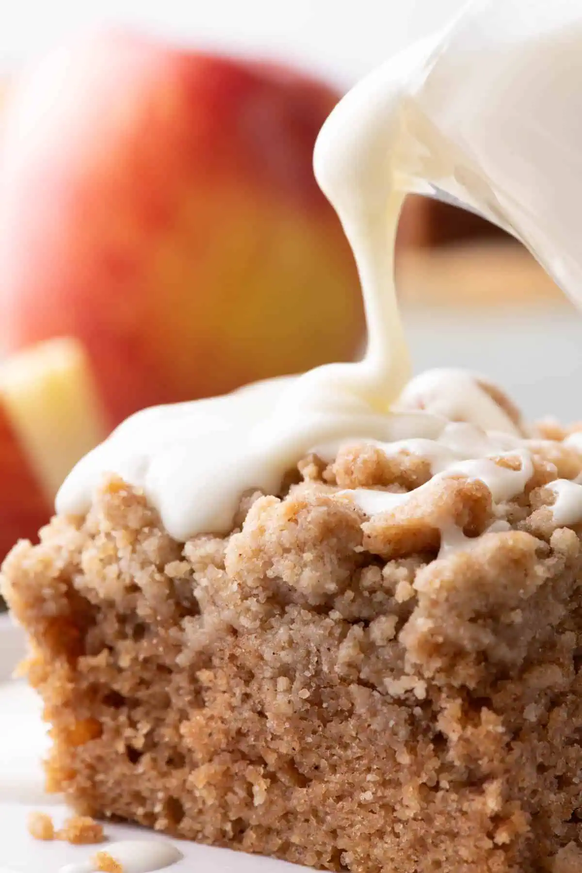 Thick cream cheese glaze being drizzled over applesauce crumb cake.