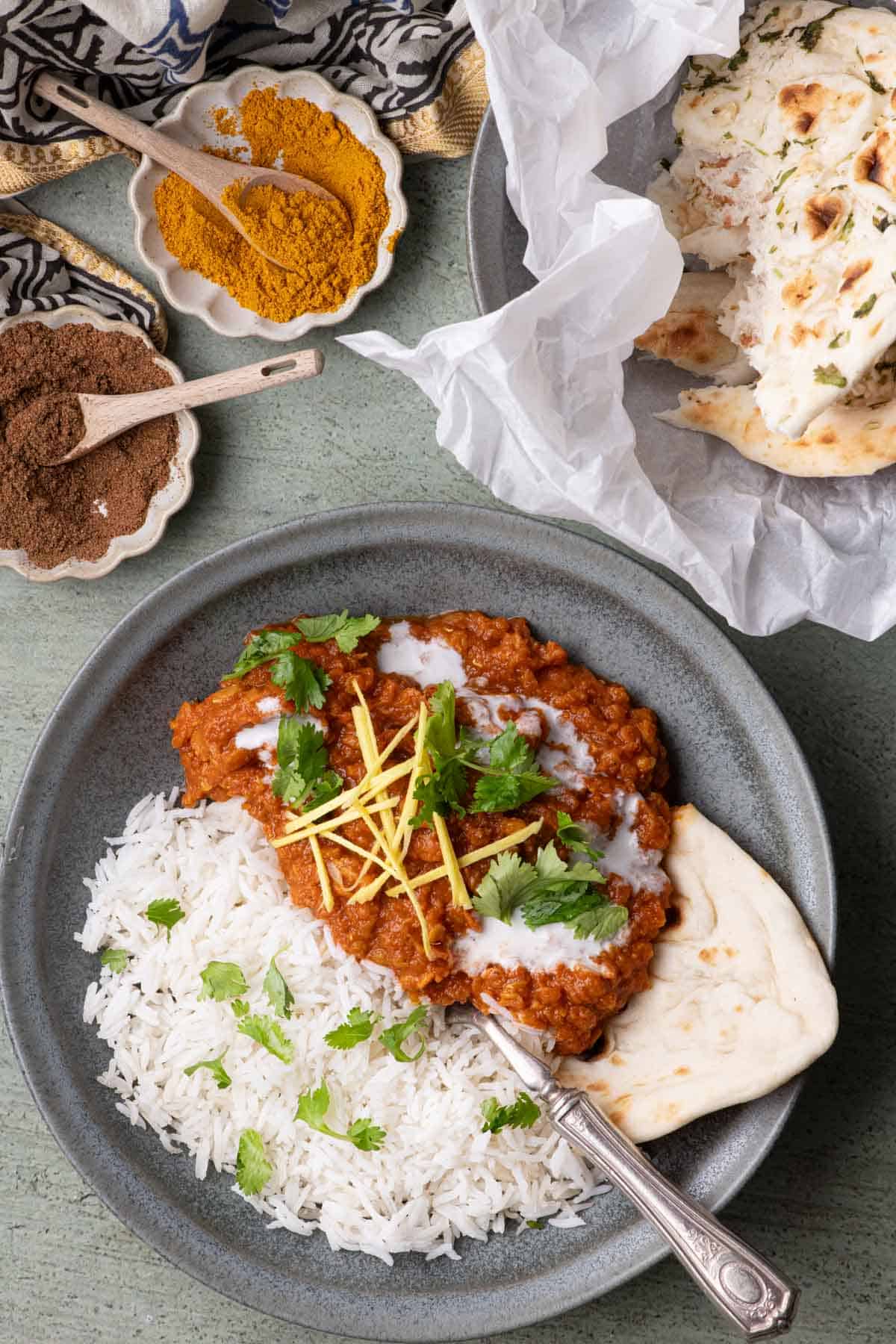 Bowl of red lentil stew served with basmati rice and naan, topped with coconut cream, cilantro, and fresh ginger