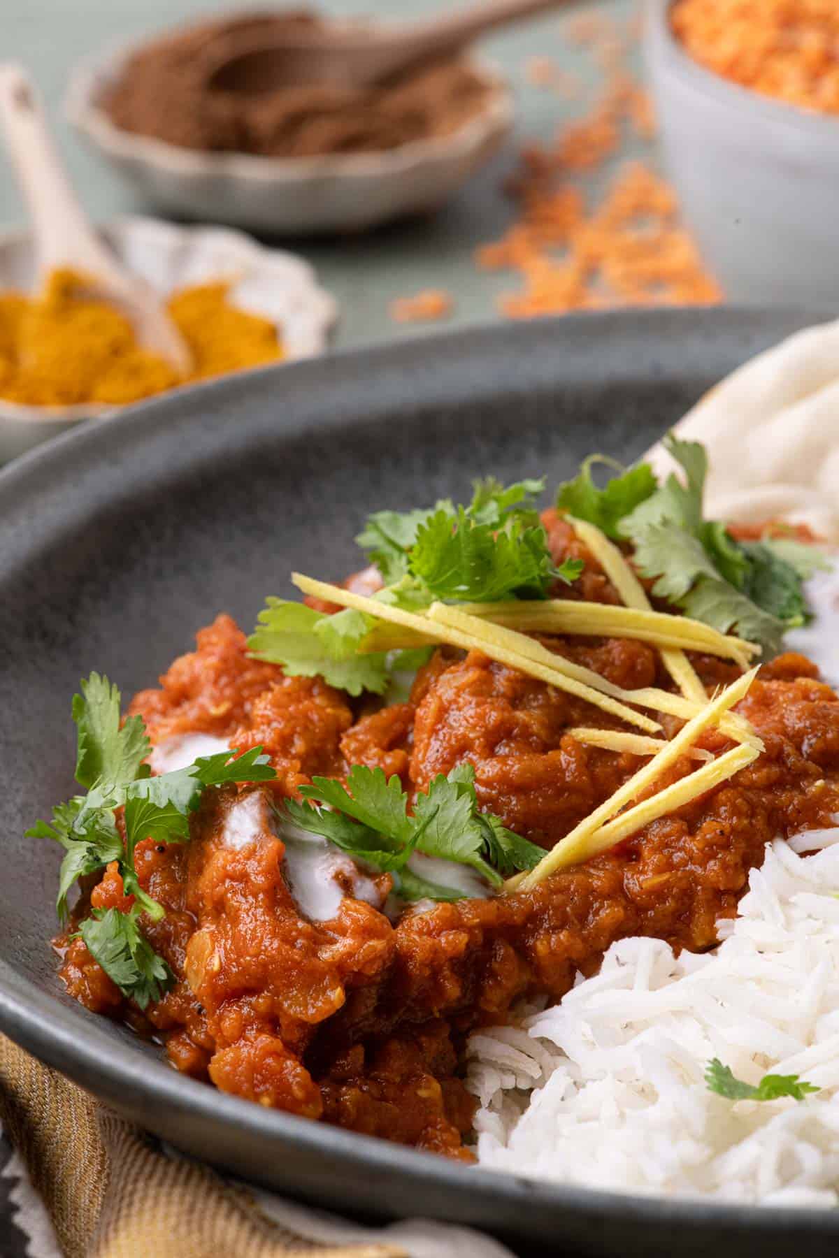 Close-up of red lentil stew with basmati rice, naan, coconut cream, cilantro, and strips of fresh ginger