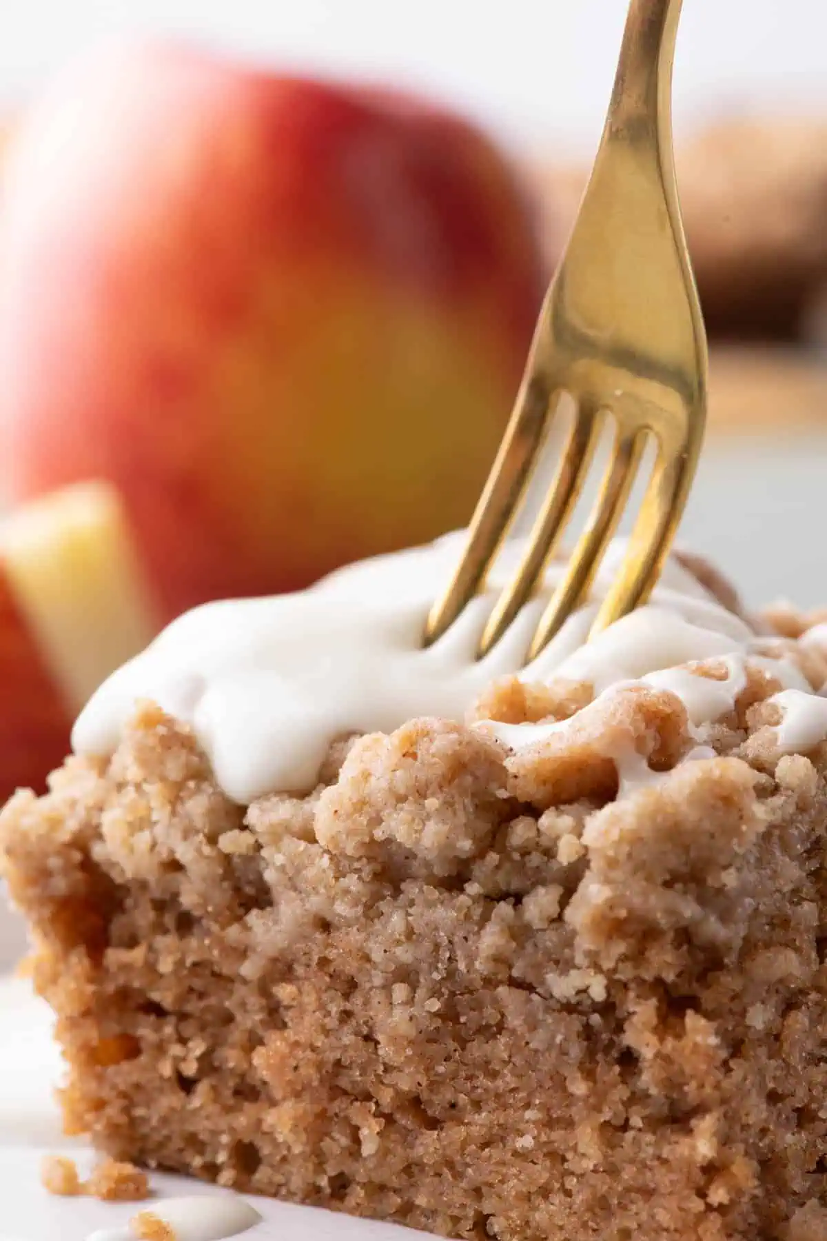 Fork cutting into applesauce crumb cake topped with thick cream cheese glaze.