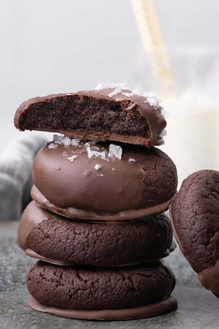 Cut chocolate dipped cookie showing its dark, soft interior resting on a stack of chocolate cookies.