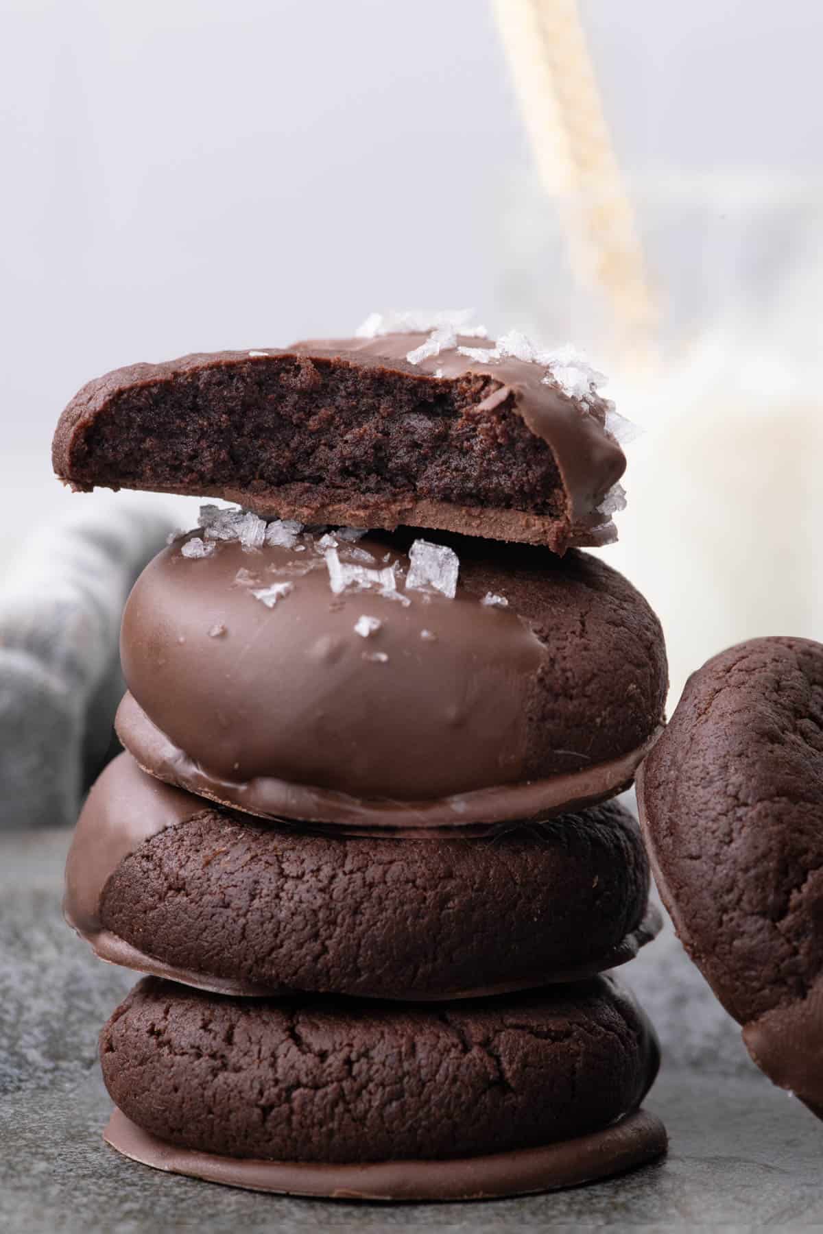 Cut chocolate dipped cookie showing its dark, soft interior resting on a stack of chocolate cookies.