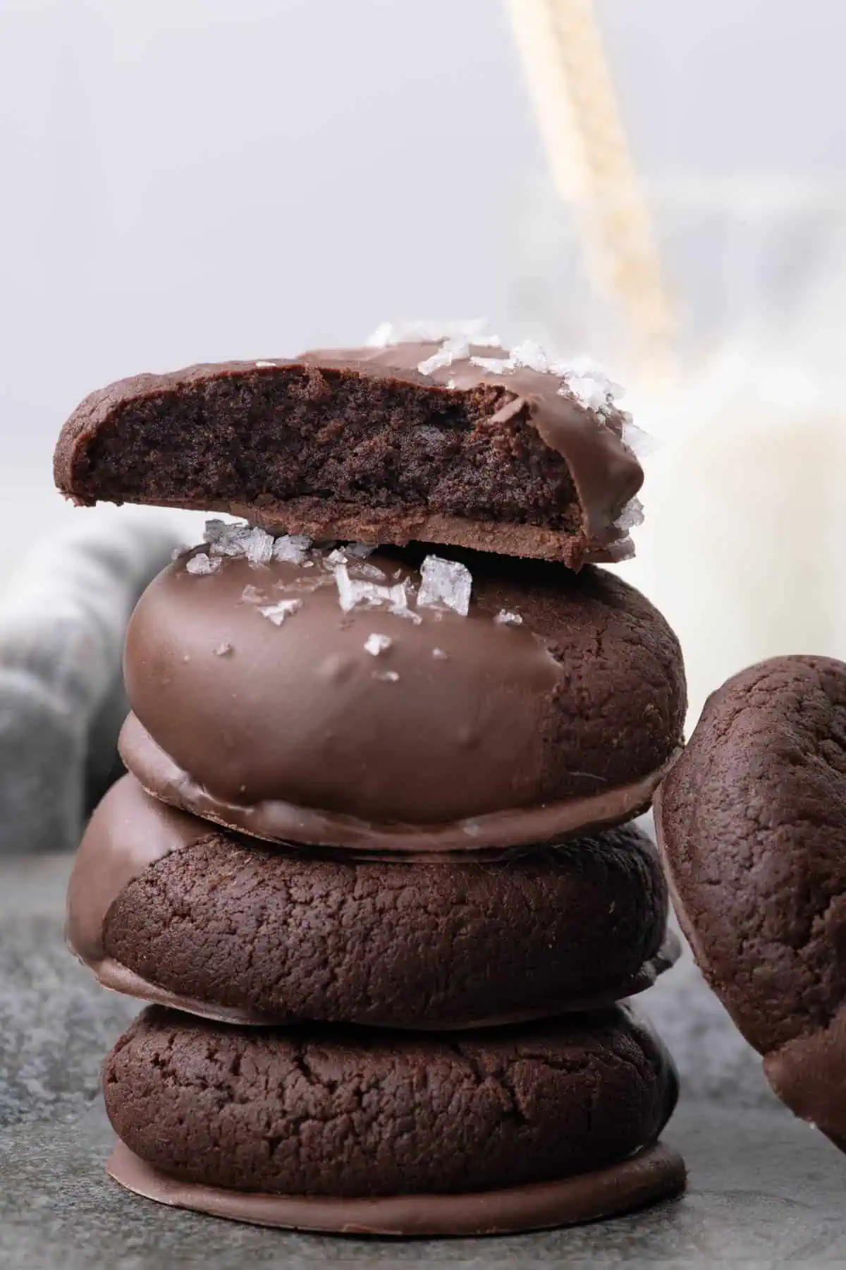 Cut chocolate dipped cookie showing its dark, soft interior resting on a stack of chocolate cookies.