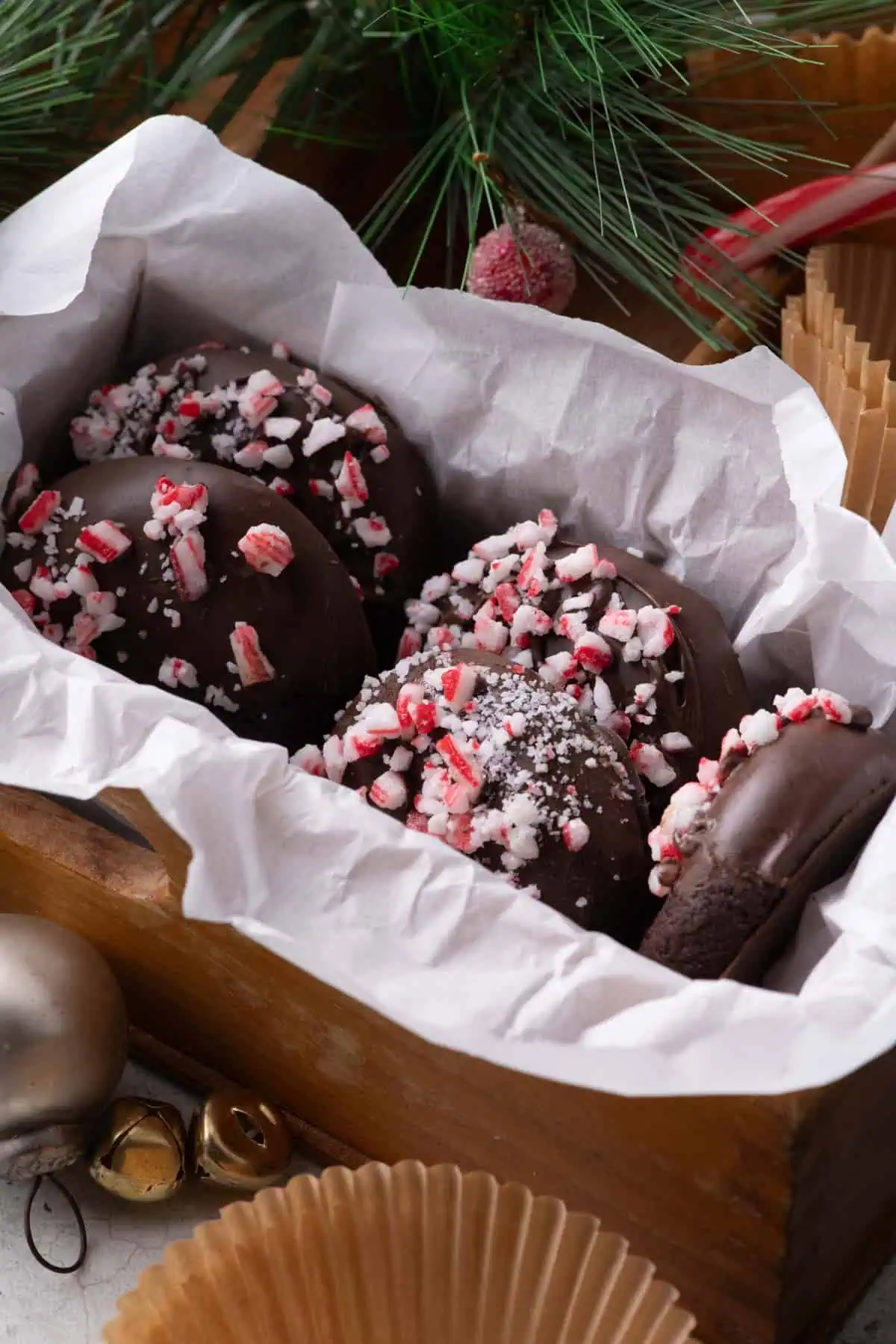 Chocolate dipped peppermint cookies arranged in a parchment-lined wooden Christmas cookie box with holiday greenery and ornaments.