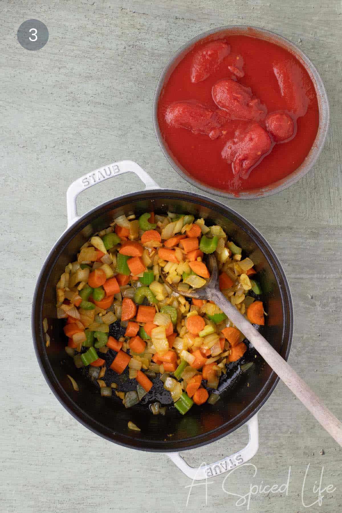 Softened vegetables in a Dutch oven with canned whole tomatoes ready to be added for spiced red lentil stew