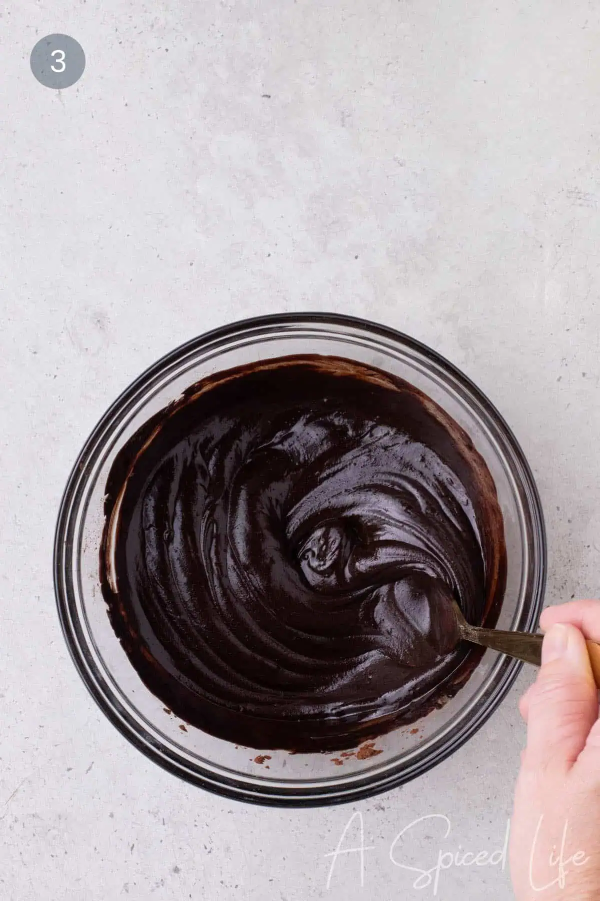 Smooth glossy chocolate mixture being stirred with a spoon in a glass bowl.