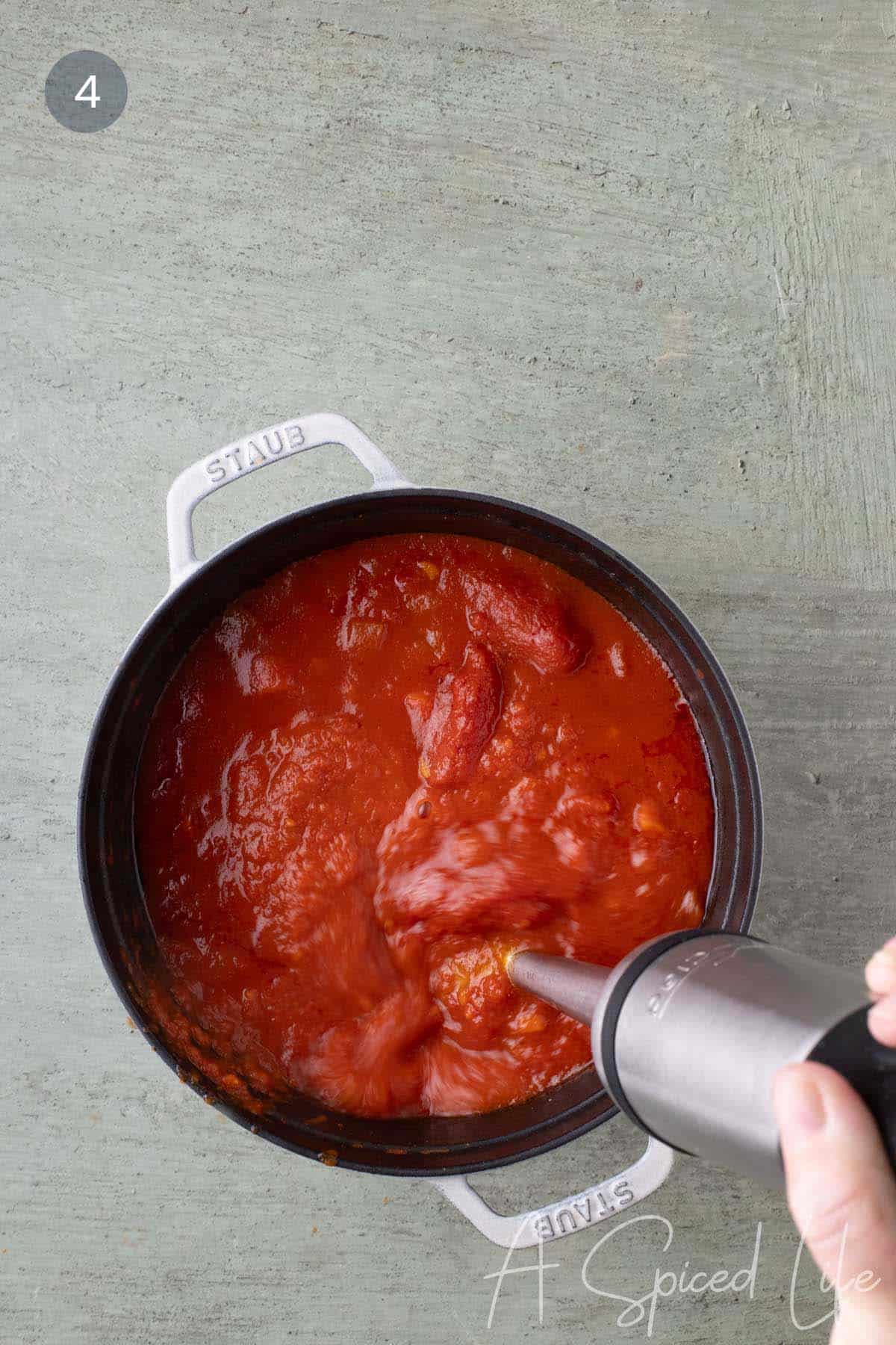 Immersion blender blending the cooked tomato and vegetable mixture in a Dutch oven until smooth