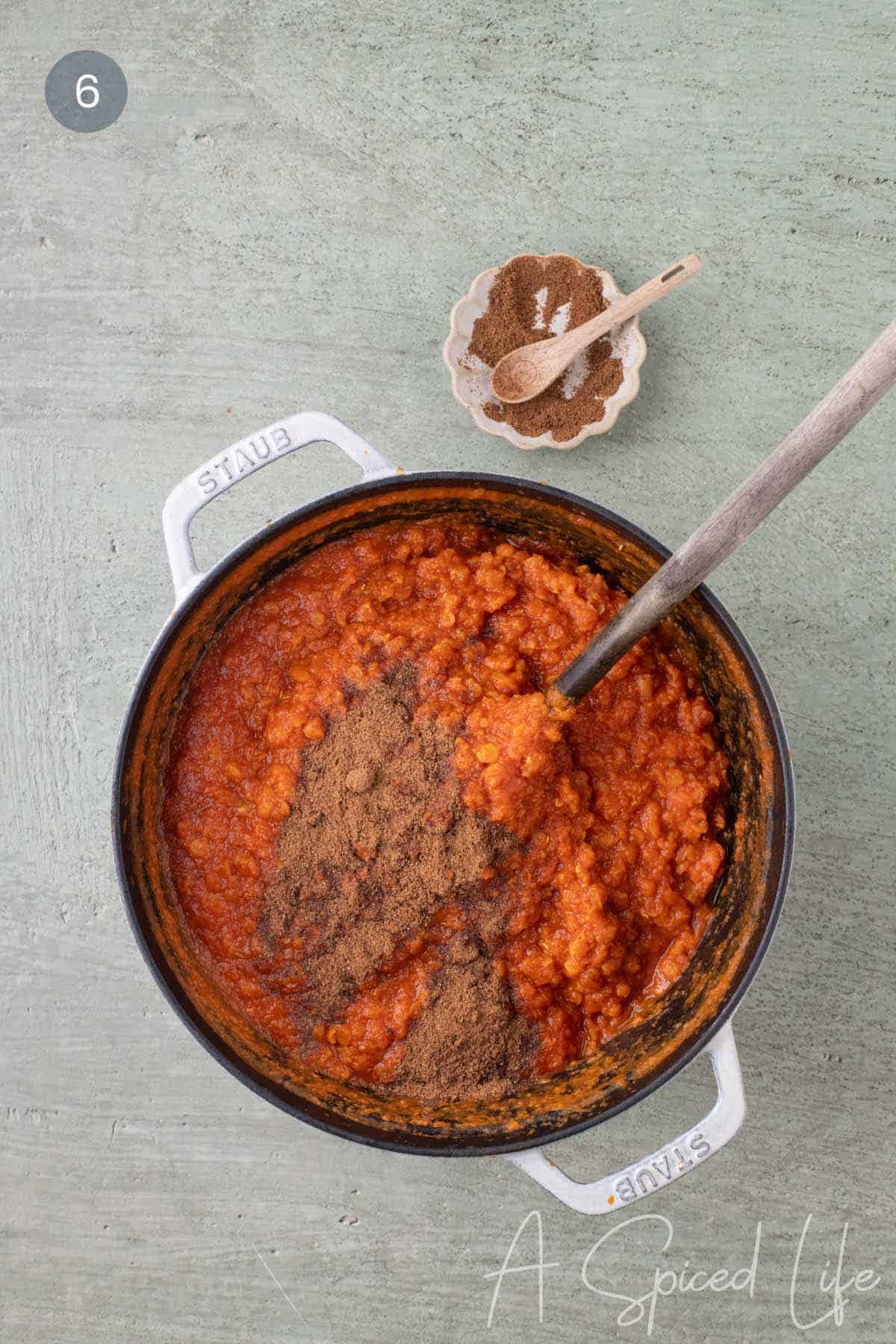 Garam masala added to cooked red lentil stew in a Dutch oven just before serving